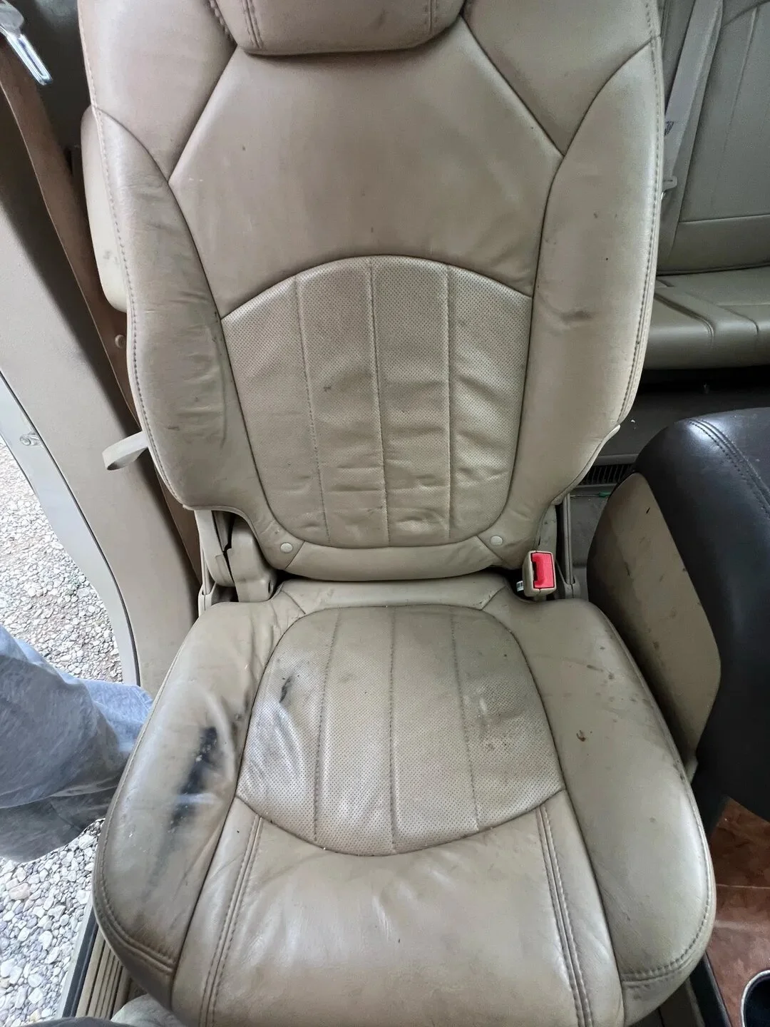 A worn beige leather seat with visible stains, dirt, and signs of aging, located inside a vehicle or similar setting.