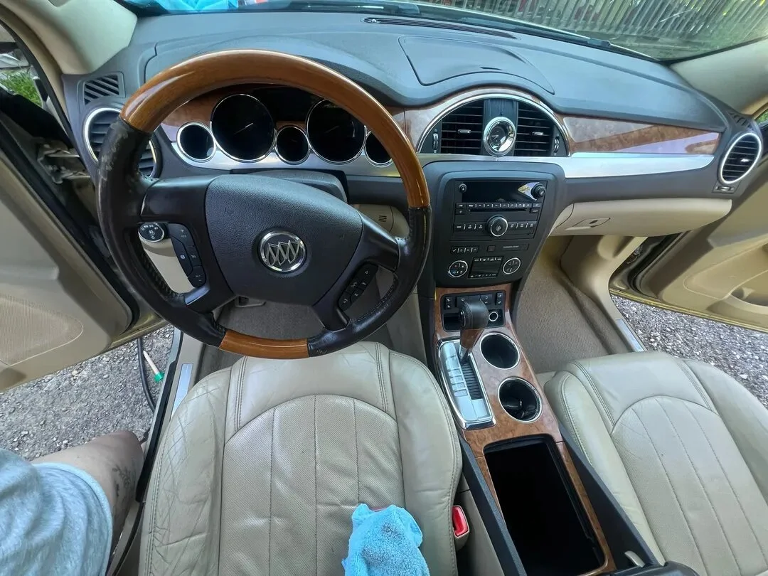 Interior view of a luxury car with a wooden steering wheel, beige leather seats, and a dashboard with wood trim and black controls.