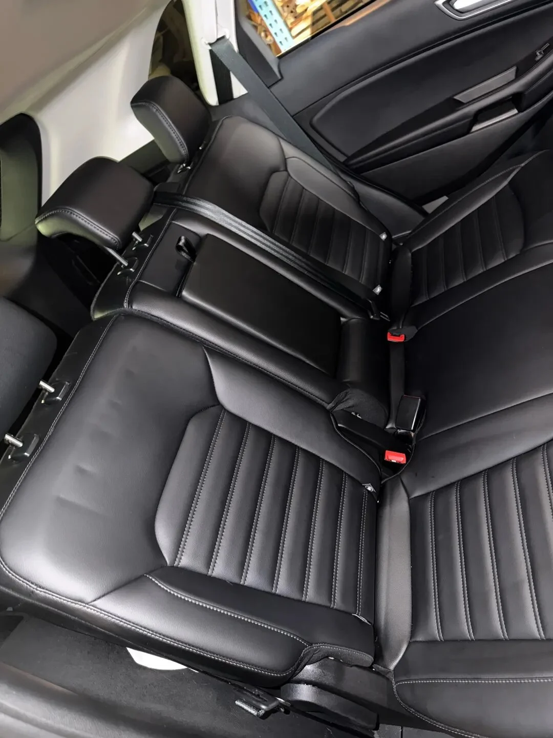 The image shows the interior of a vehicle with black leather seats, including the back seats and headrests, with five seat belts visible.