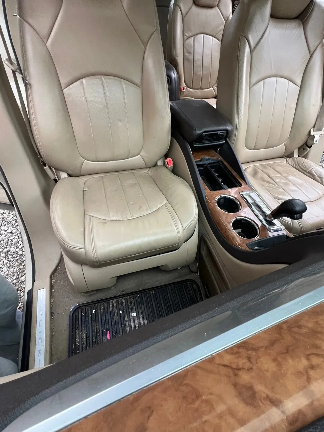 Interior of a vehicle showing beige leather seats, a center console with wooden accents, cup holders, gear shifter, and an armrest.