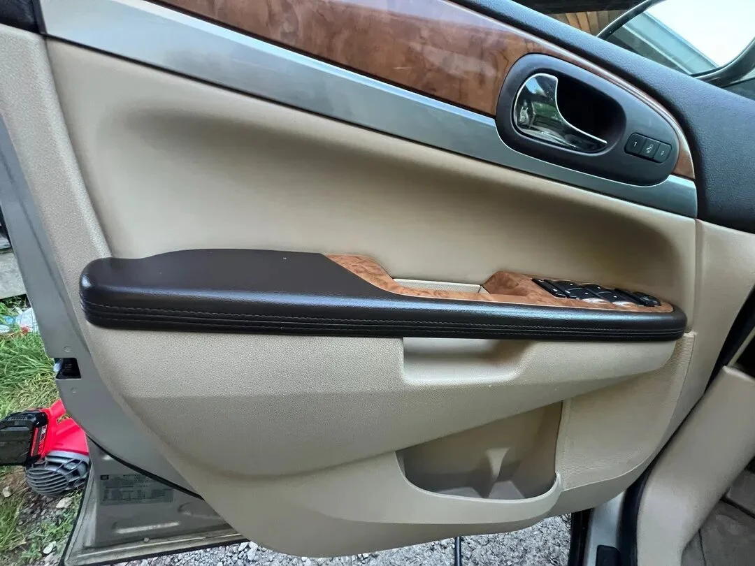 Close-up of a car door interior with beige and black trim, wood accents, window control buttons, and a door handle.