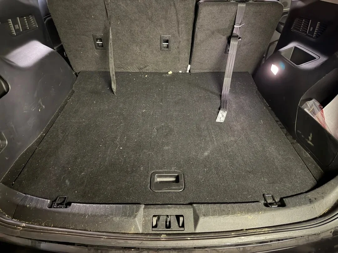 Empty cargo area of a vehicle with a raised back seat, featuring some dirt and debris on the carpeted floor.
