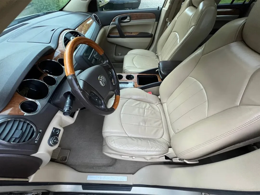 Front interior of a car showing beige leather seats, a woodgrain steering wheel, and a dashboard with woodgrain accents and round air vents.