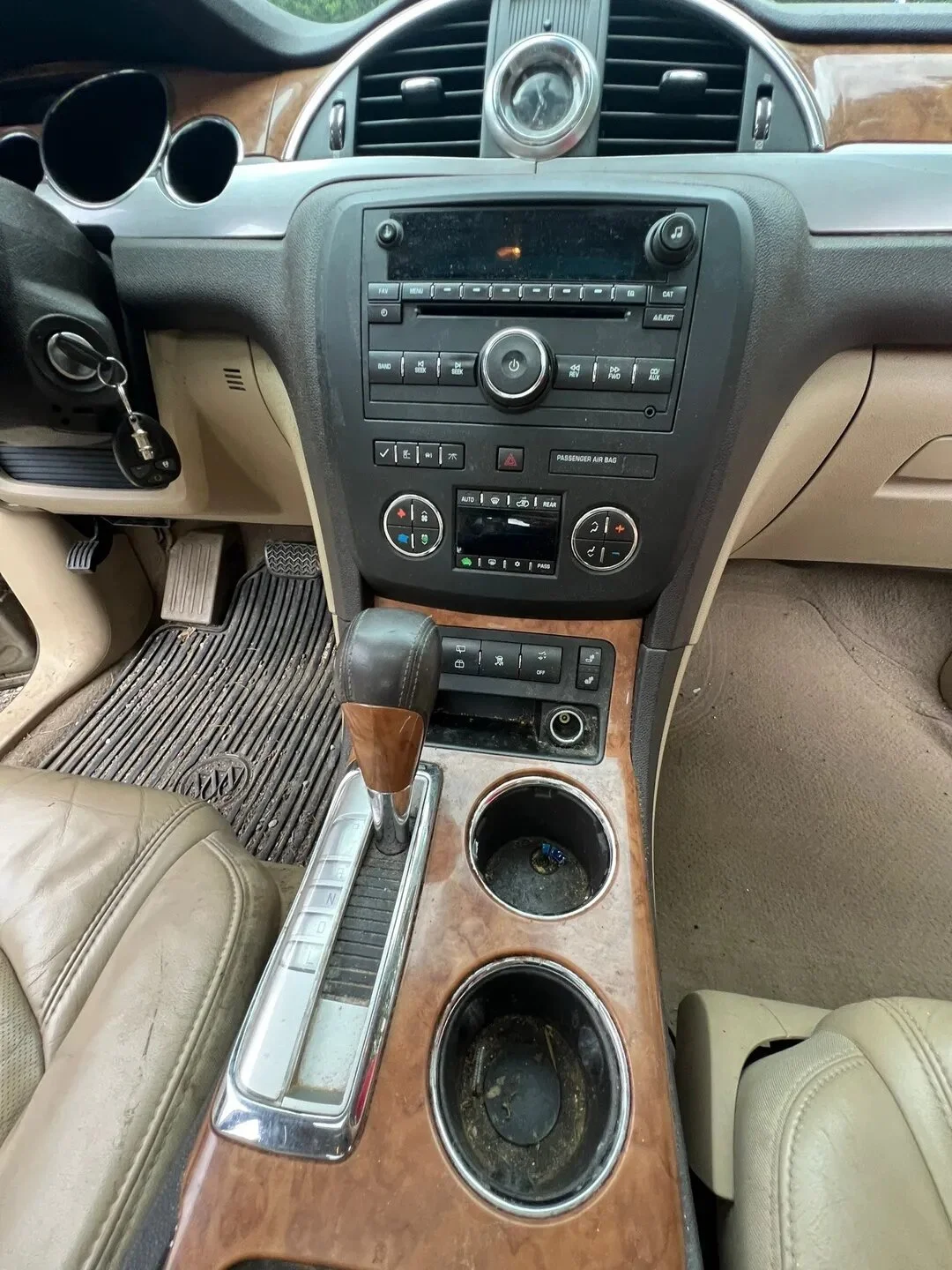 The interior of a car showing the dashboard, center console with cup holders, gear shift, and beige leather seats. The dashboard includes a radio, climate controls, and various buttons.