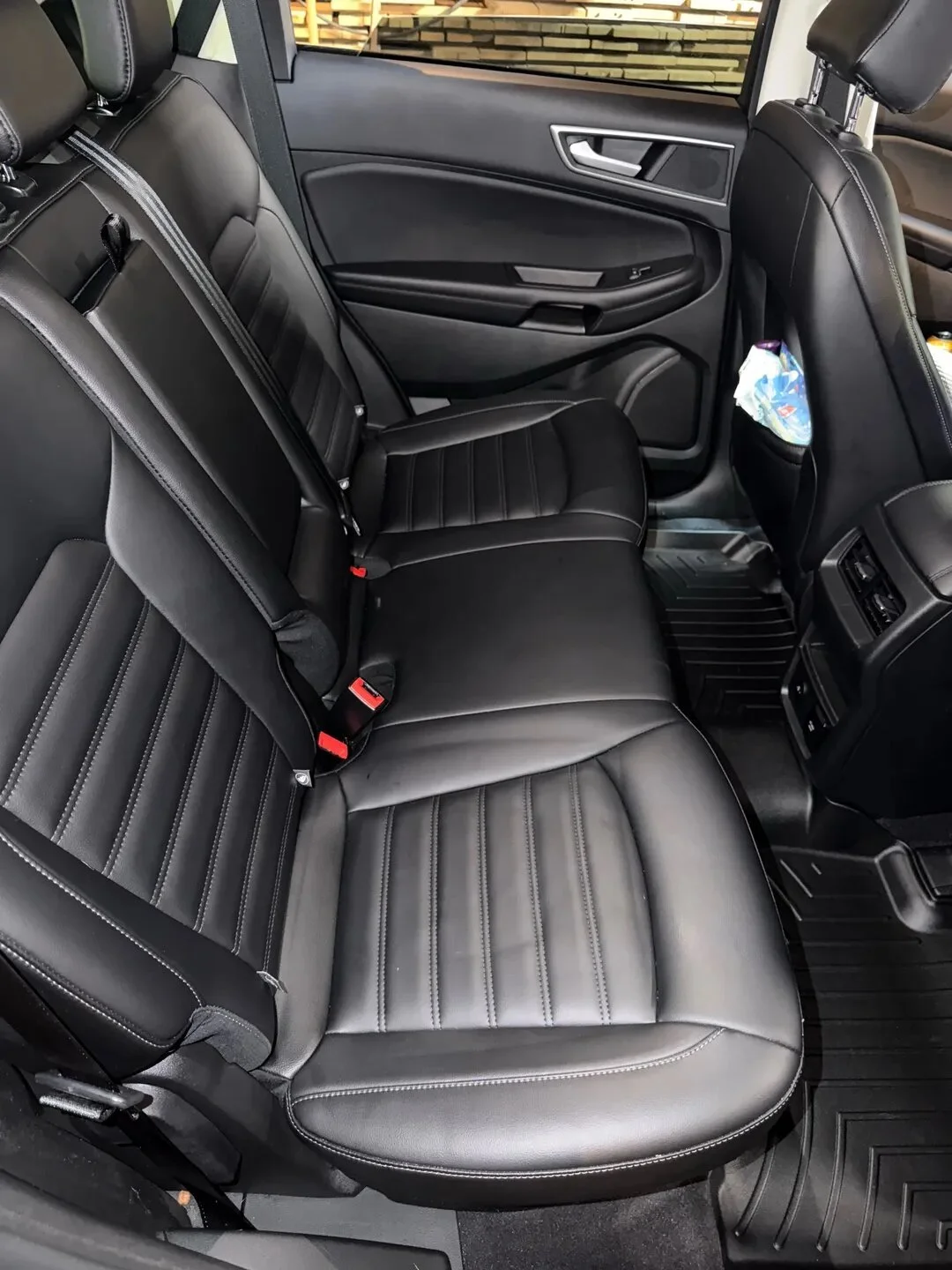 Back seat of a car with black leather seats, black door panel, and a window with a view of outside.