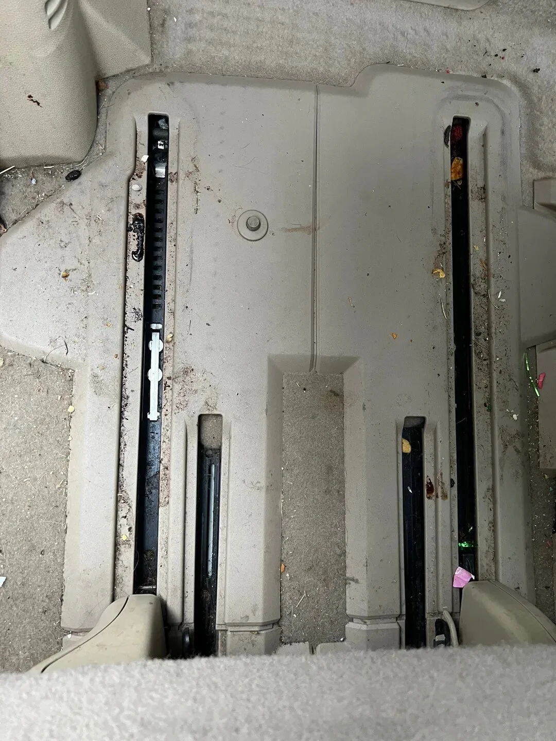 The view of a dirty and empty car floor with removed seat, showing the metal brackets and mechanisms underneath.