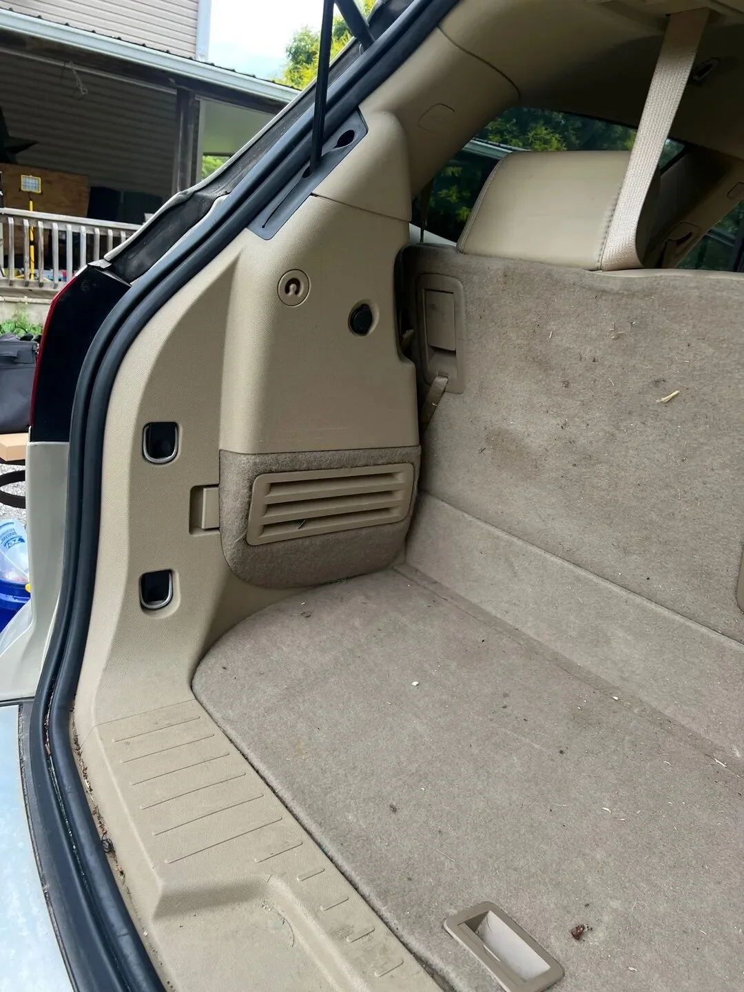 The cargo area of an SUV with beige interior, showing a flat floor, folded rear seats, and a small plastic compartment on the left side.