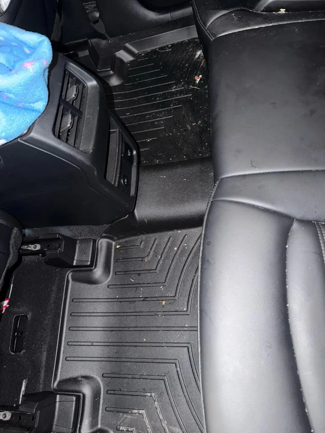 Car interior showing black rubber floor mats with dirt and debris, and part of a black leather seat.