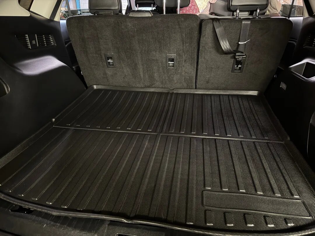 The interior cargo area of an SUV with a fitted black rubber cargo mat and the back seats in an upright position.