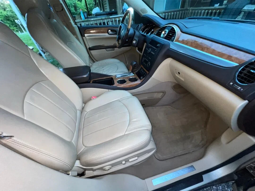 Interior of a vehicle showing beige leather seats, wooden dashboard accents, and a steering wheel, with the driver's seat and part of the passenger seat visible.