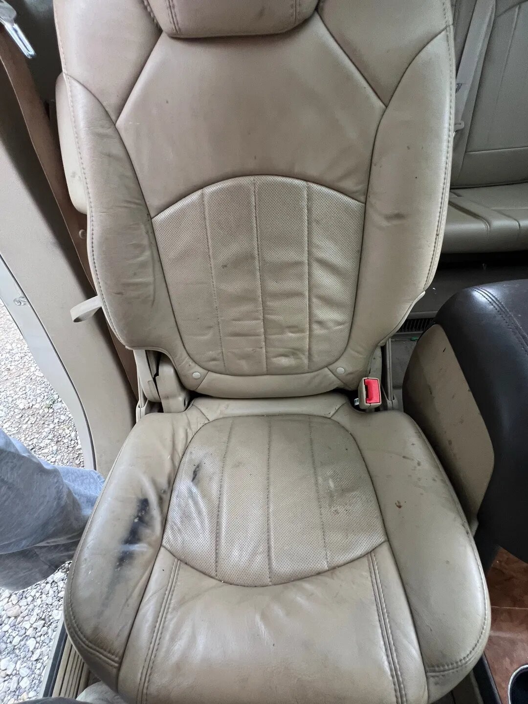 Dirty beige leather airplane or vehicle seat with visible stains and damage.