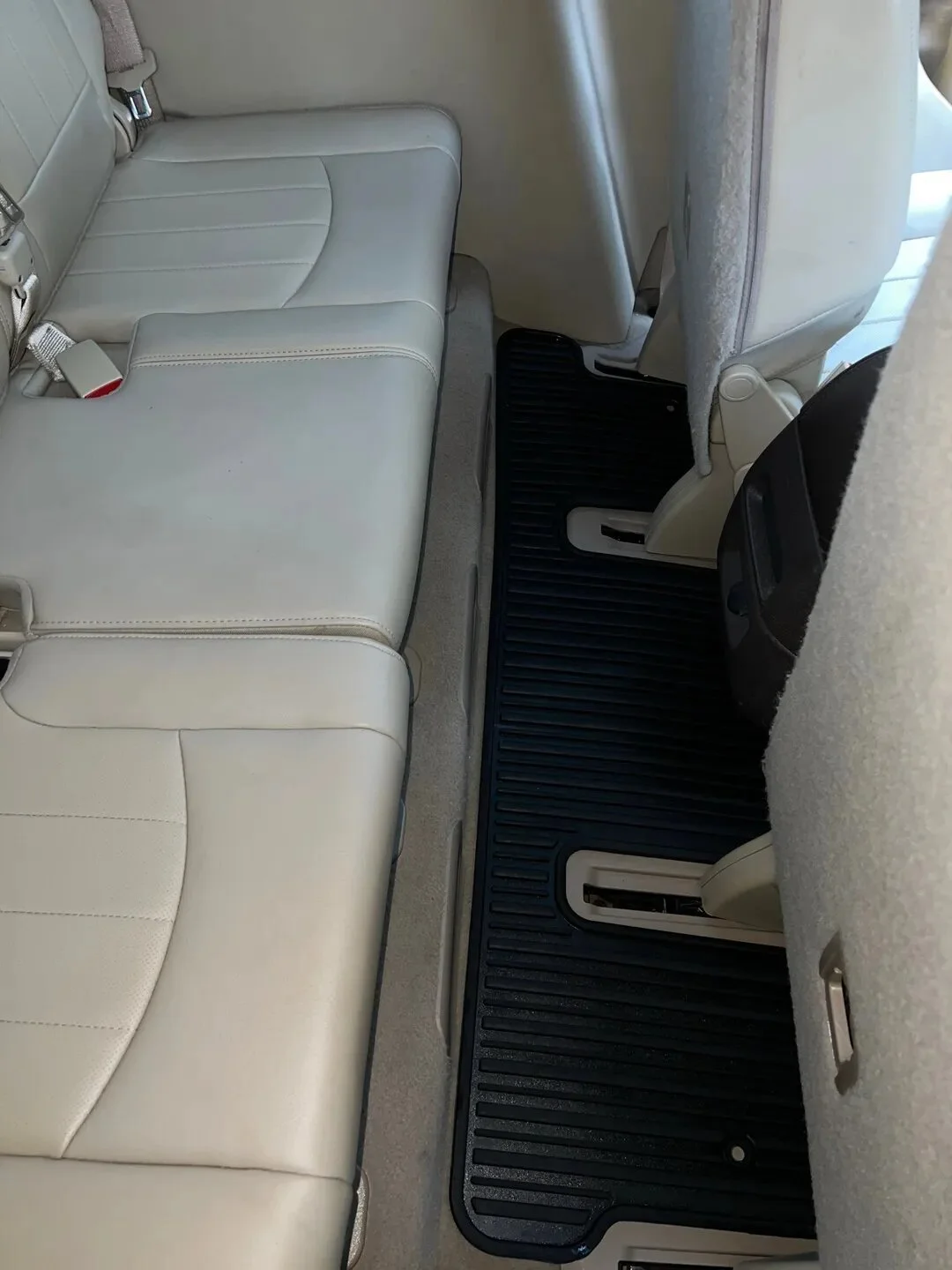 View of the back seat of a vehicle with beige leather seats and a black rubber floor mat.