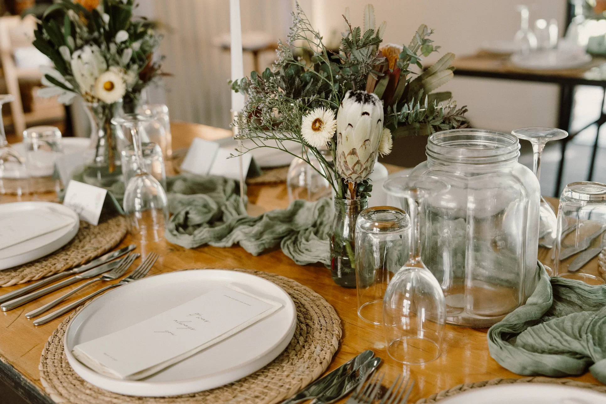 A table set for a meal with a centerpiece of cacti and white daisy flowers; round white plates with napkins, glassware, and cutlery are arranged around the table.