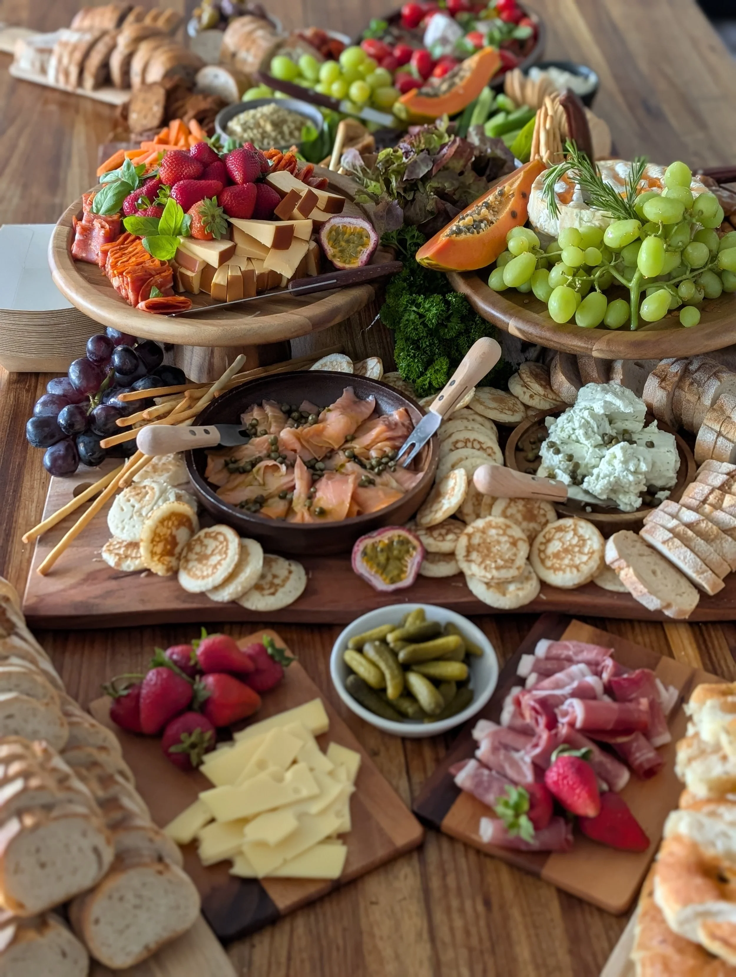 A variety of food items arranged on wooden boards and platters, including cheese, grapes, strawberries, crackers, sliced meats, vegetables, and dips, forming a charcuterie board spread.