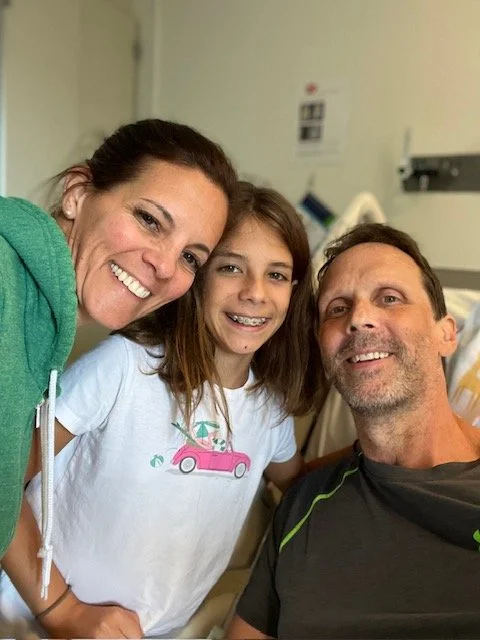 A woman, a young girl, and a man smiling for a photo in a hospital room.