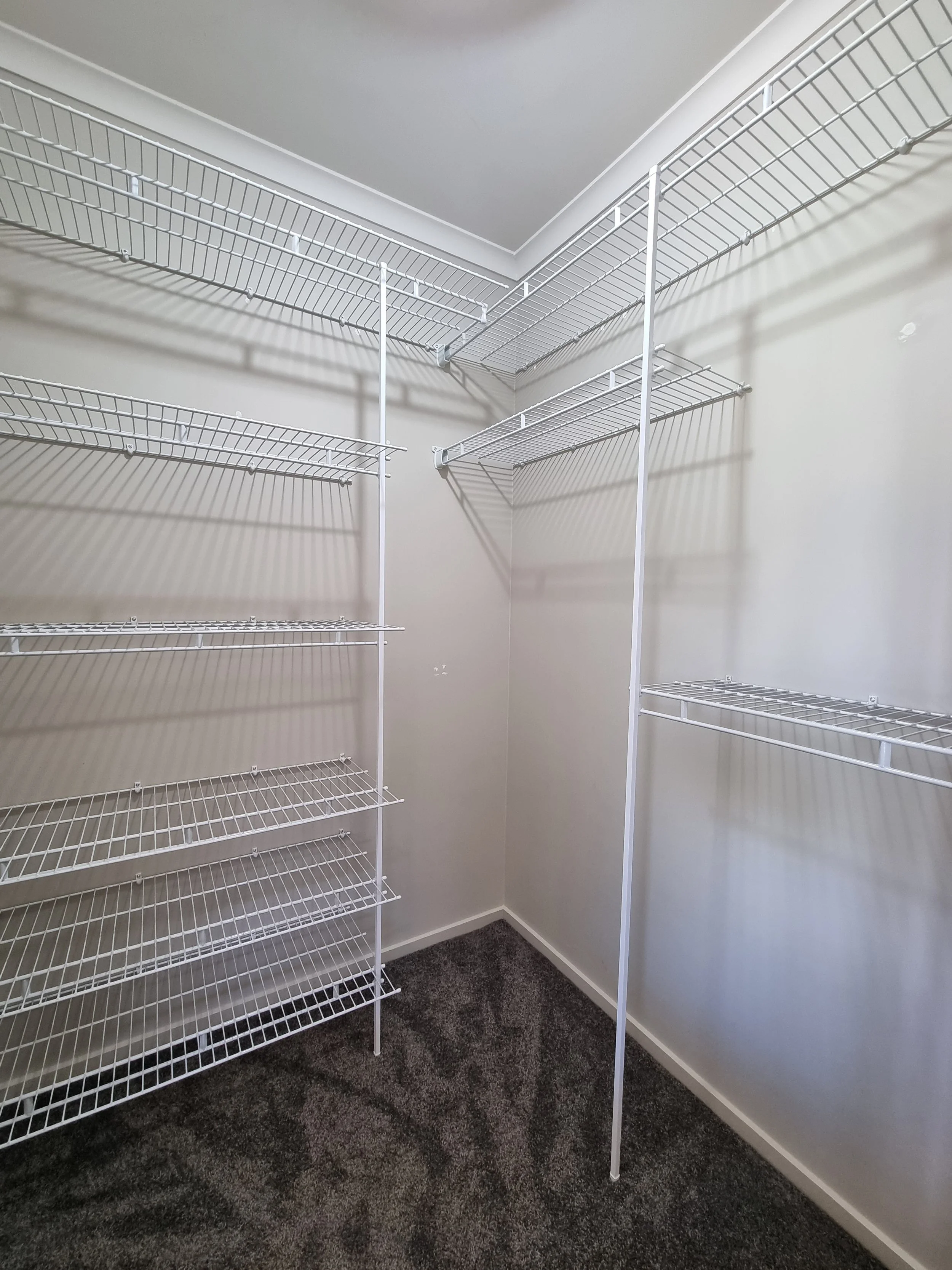 Empty white wire shelving in a small closet with dark carpeted floor.