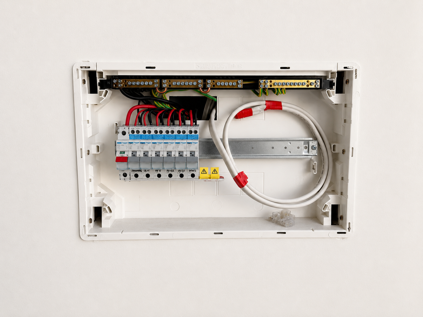 Open electrical panel with circuit breakers, wires, and connectors mounted on a white wall.
