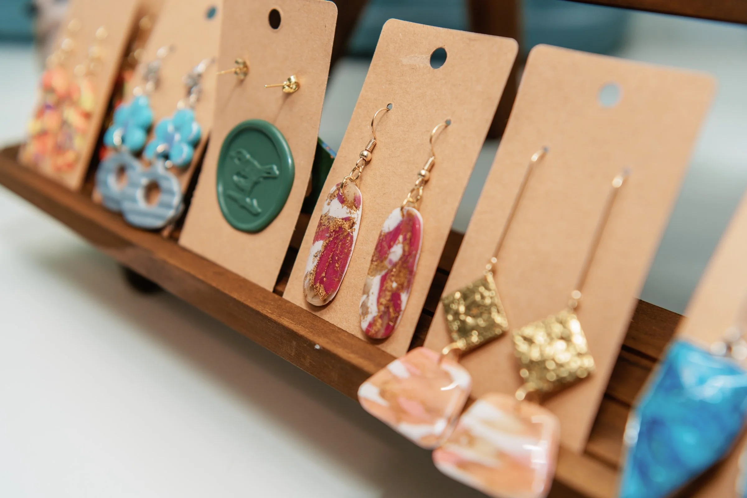 Close-up of a display rack with various colorful earrings on cardboard backing, arranged in a row.