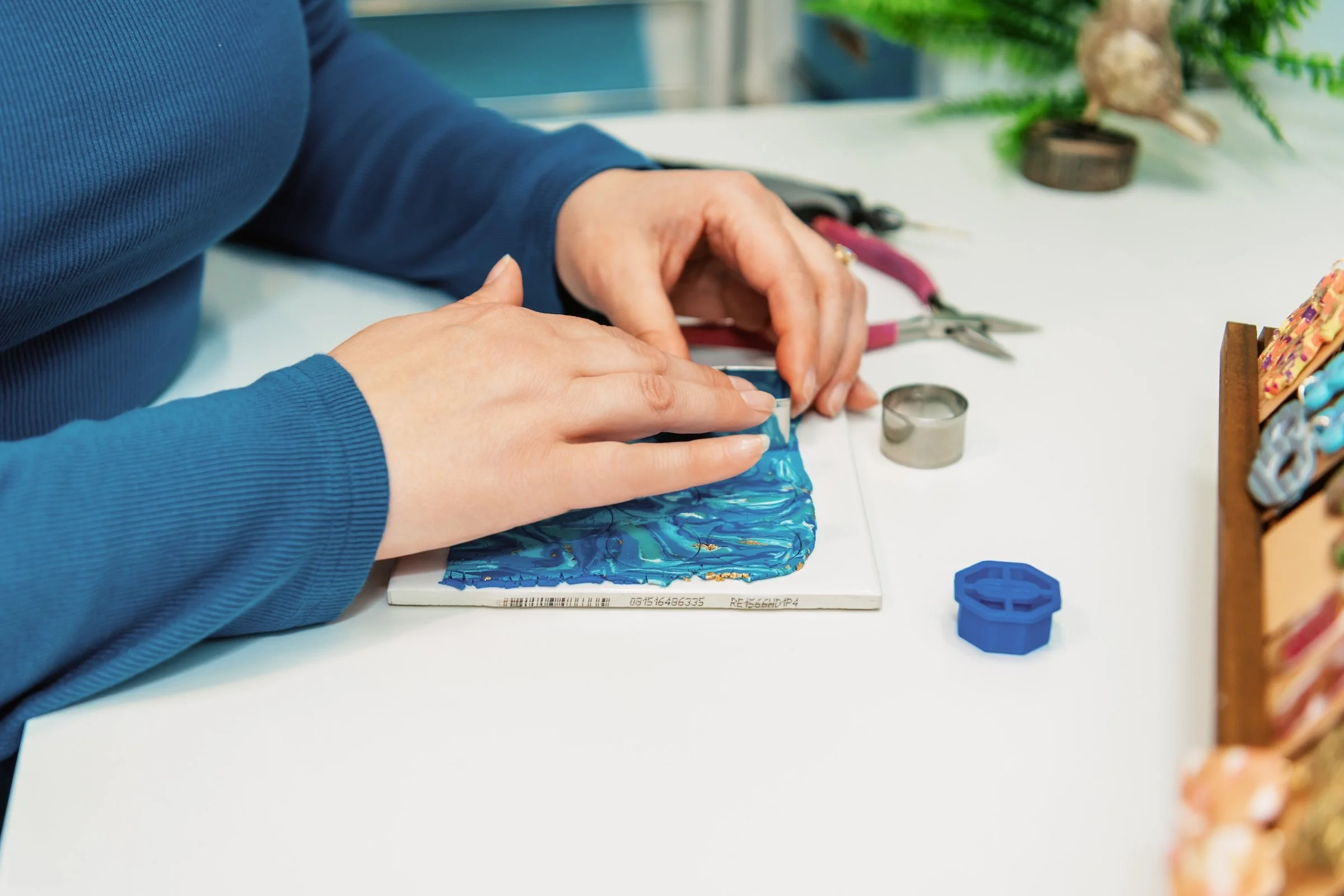 A person on a colorful resin craft project at a white table, with various crafting tools and supplies nearby.