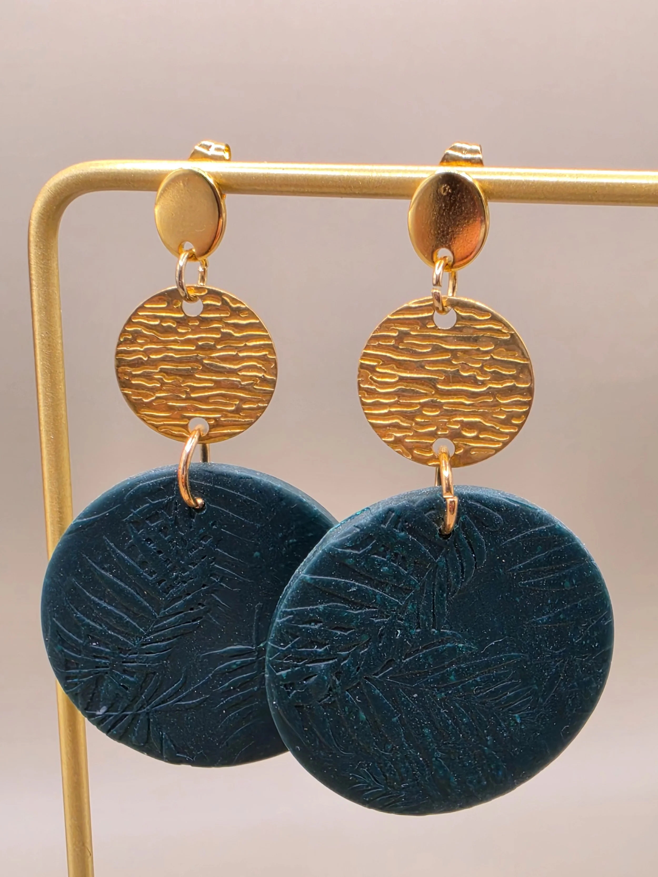 Gold and dark blue circular earrings displayed on a gold stand.