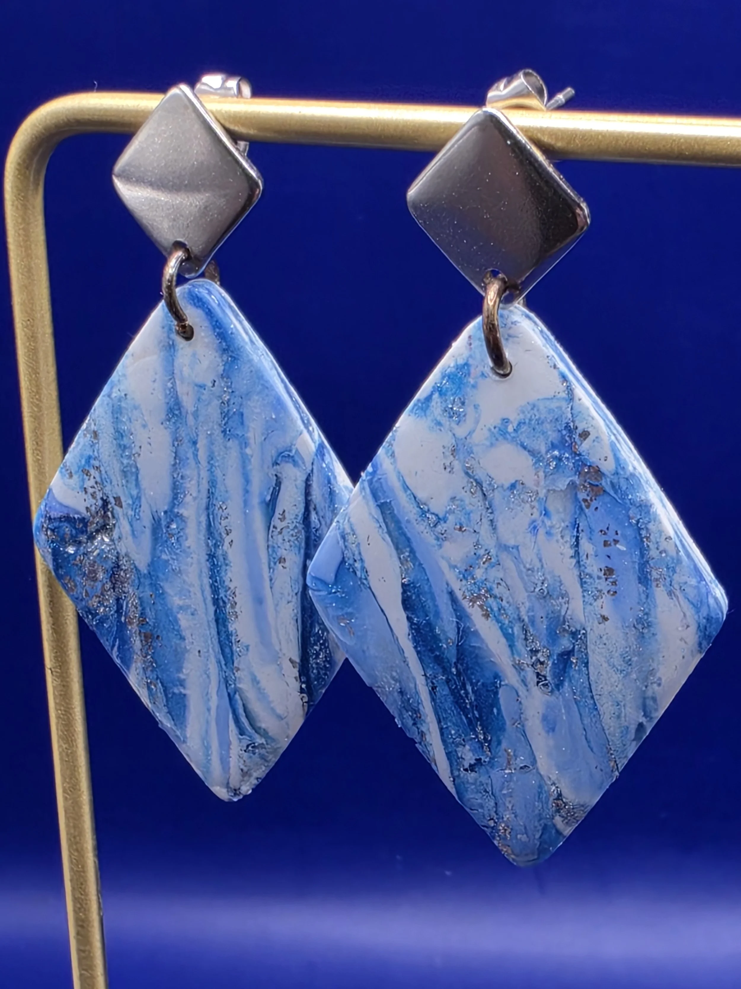 Blue and white marbled earrings hanging from a metal display stand against a blue background.