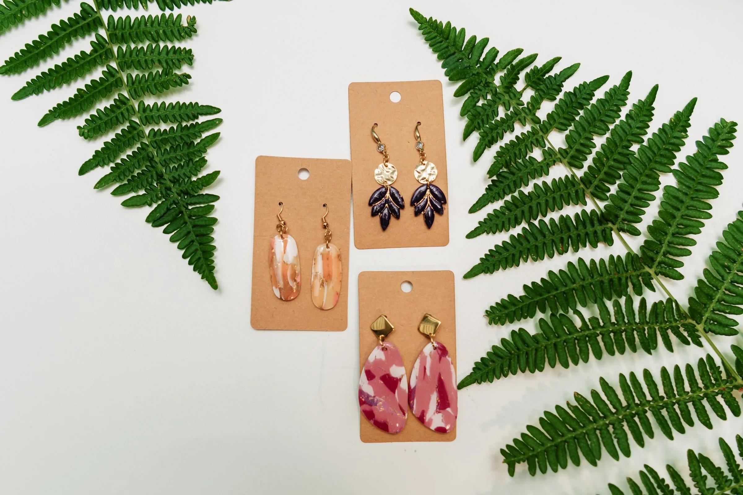 Assorted earrings displayed on cardboard tags, surrounded by fern leaves.