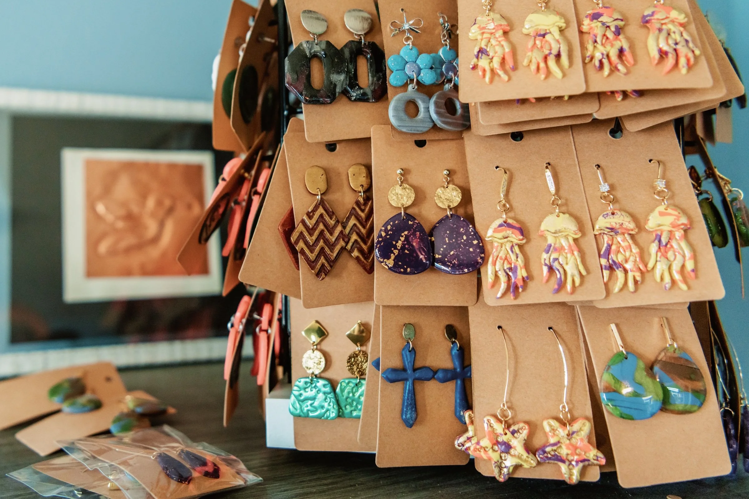 Display of various colorful earrings on a jewelry stand, including floral, geometric, and abstract designs.