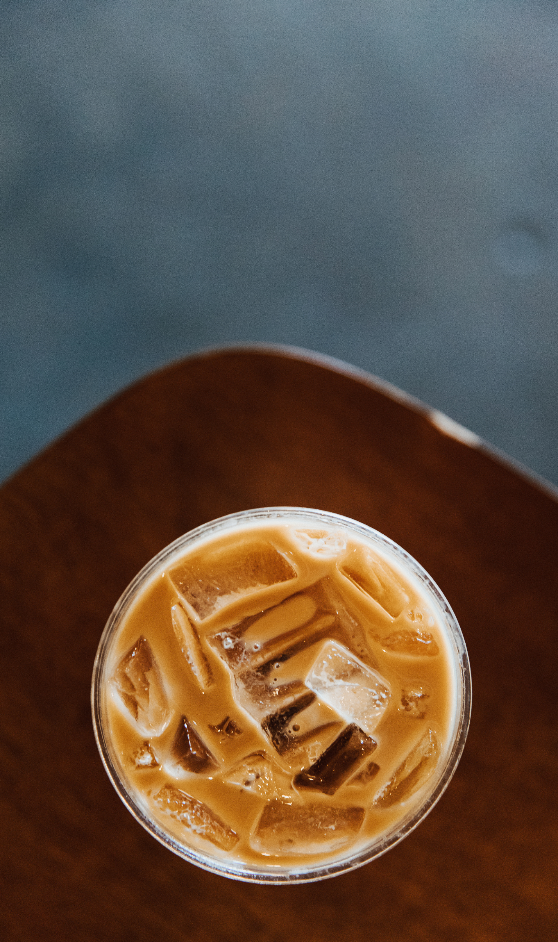 Top-down view of a glass of iced coffee with milk on a wooden table, with a gray background.