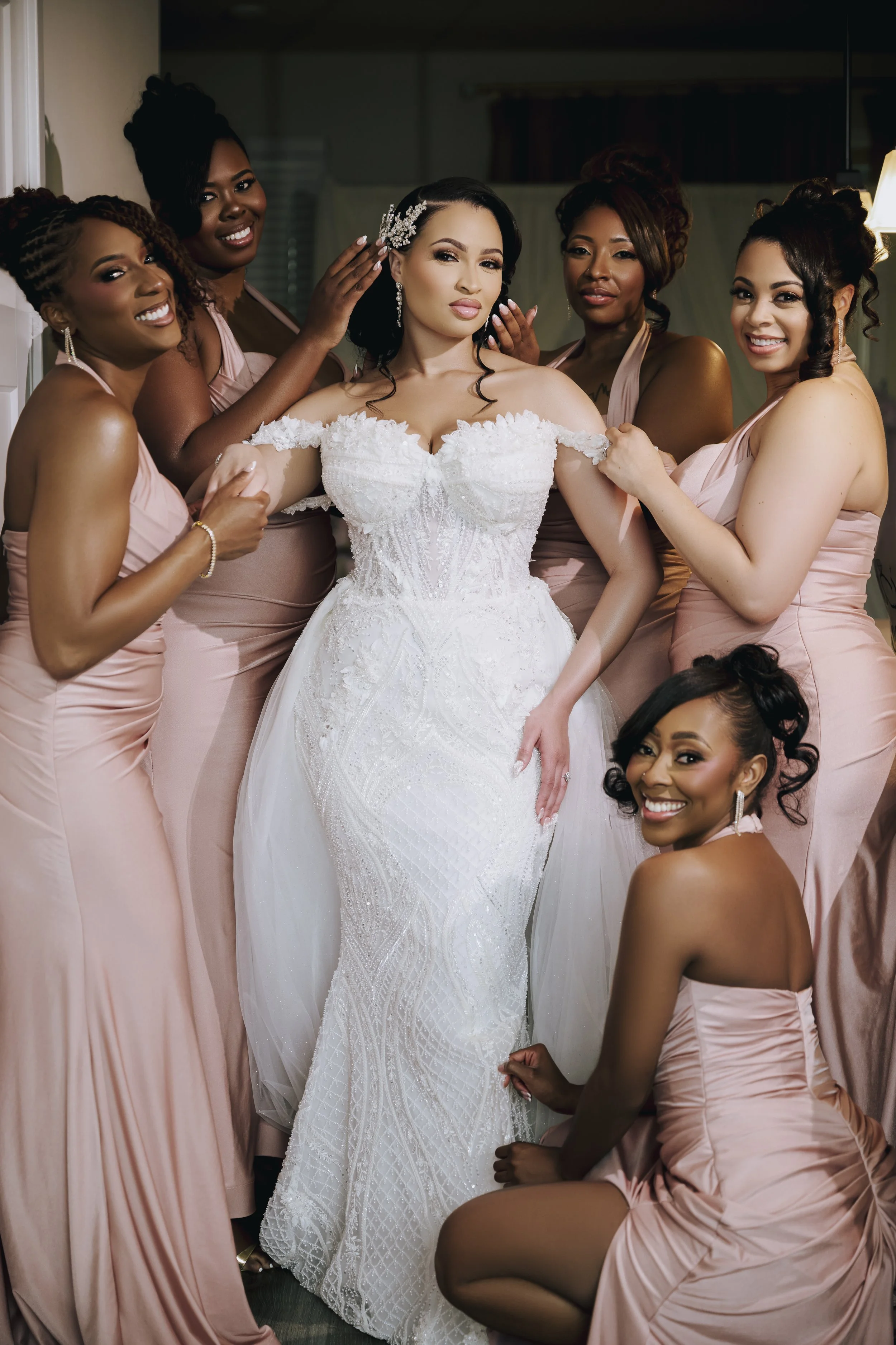 A bride in a white wedding dress surrounded by five bridesmaids in light pink dresses.