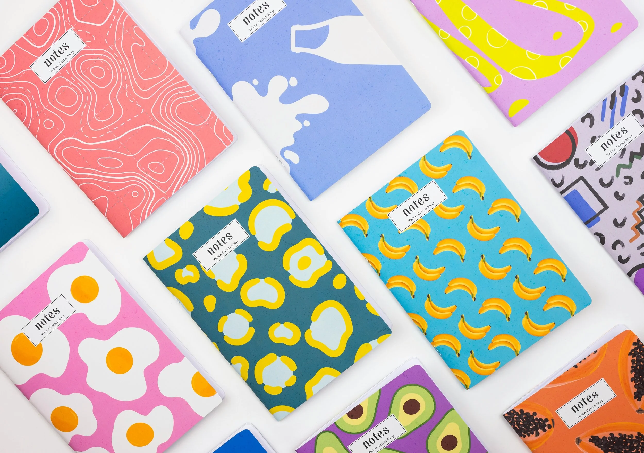 A collection of colorful notebooks with various abstract and playful designs on their covers, laid out flat on a white surface.