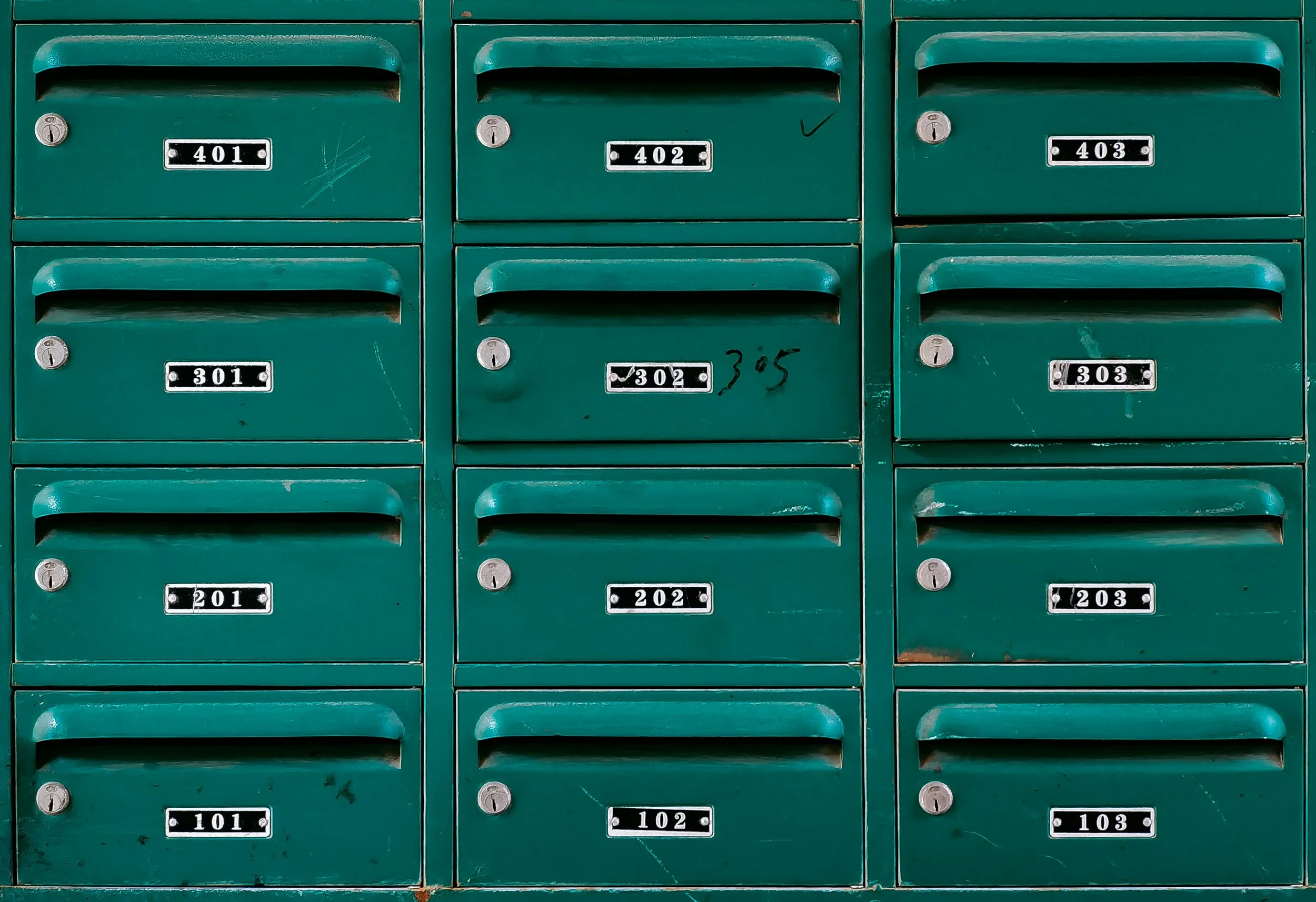 Green mailboxes with black and white number plates, arranged in three columns and four rows, with keys in some locks.