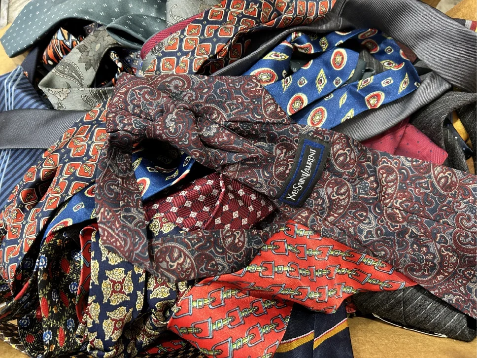 A collection of various colorful ties with different patterns, including paisley, geometric, and floral designs.