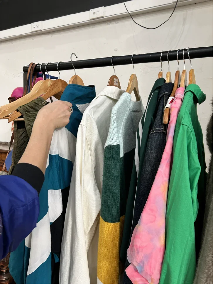 A person shopping for clothing, reaching for a striped jacket on a rack filled with various colorful jackets and hoodies.