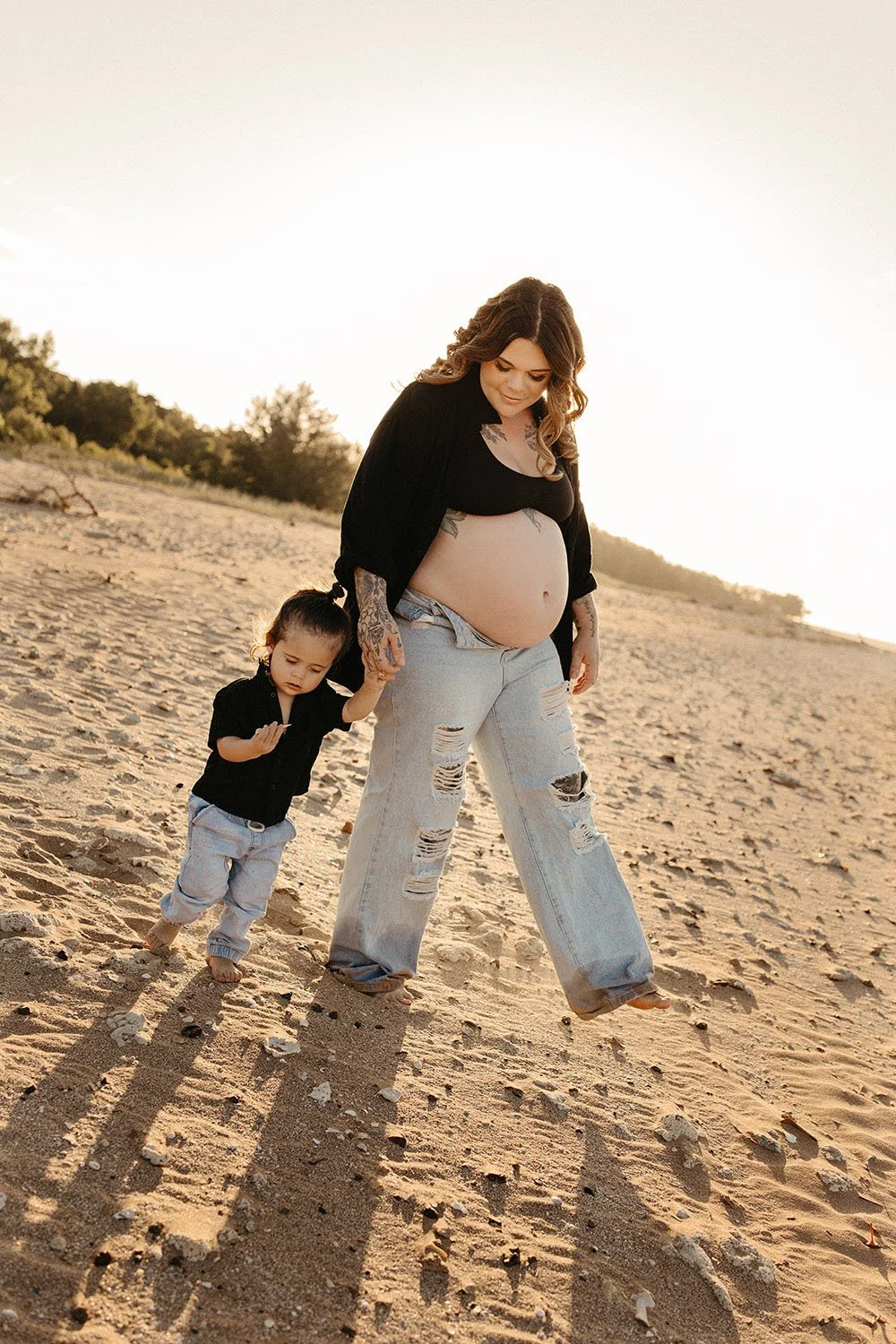 A pregnant woman on the beach at golden hour, holding her toddler's hand. Family and maternity photo shoot, Captured by Cody.
