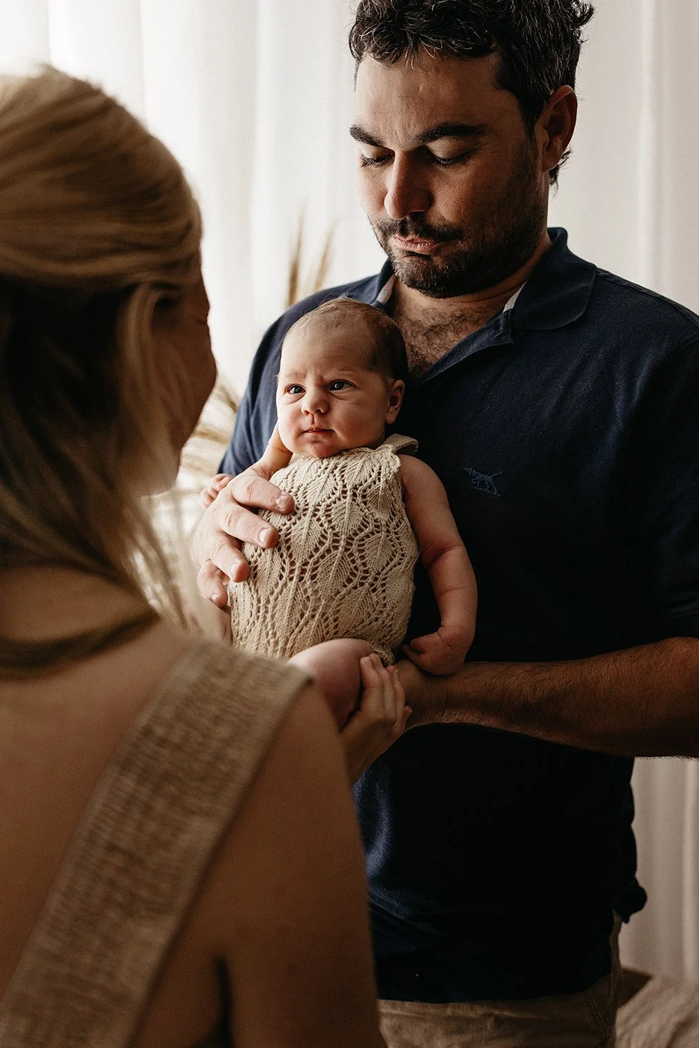 Father holding his newborn baby, looking at his mother. Studio newborn photography session, Captured by Cody, Darwin & Palmerston.