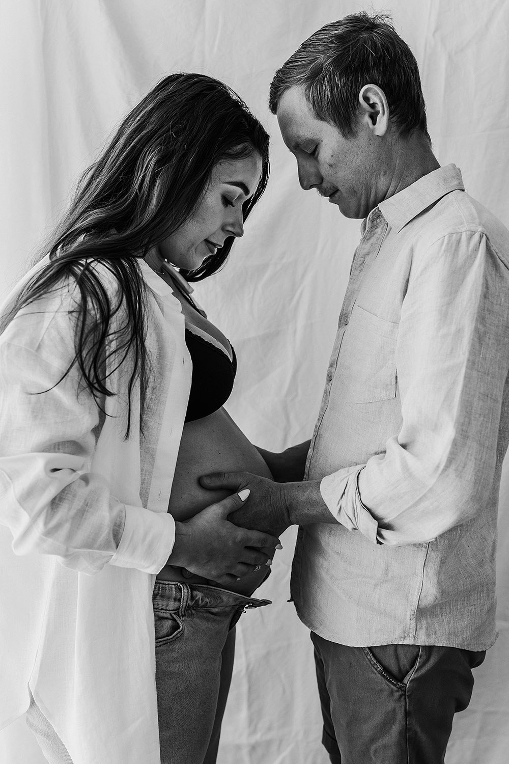 A couple at a studio maternity shoot. Father with his hands on the mother's pregnant belly. Captured by Cody family photography, Darwin, NT.