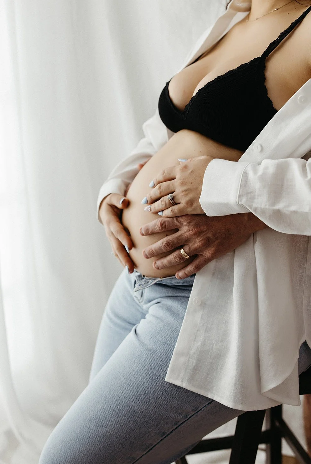 A woman in jeans and a white shirt with her hands on her pregnant belly. Studio maternity shoot, Captured by Cody, Darwin, NT.