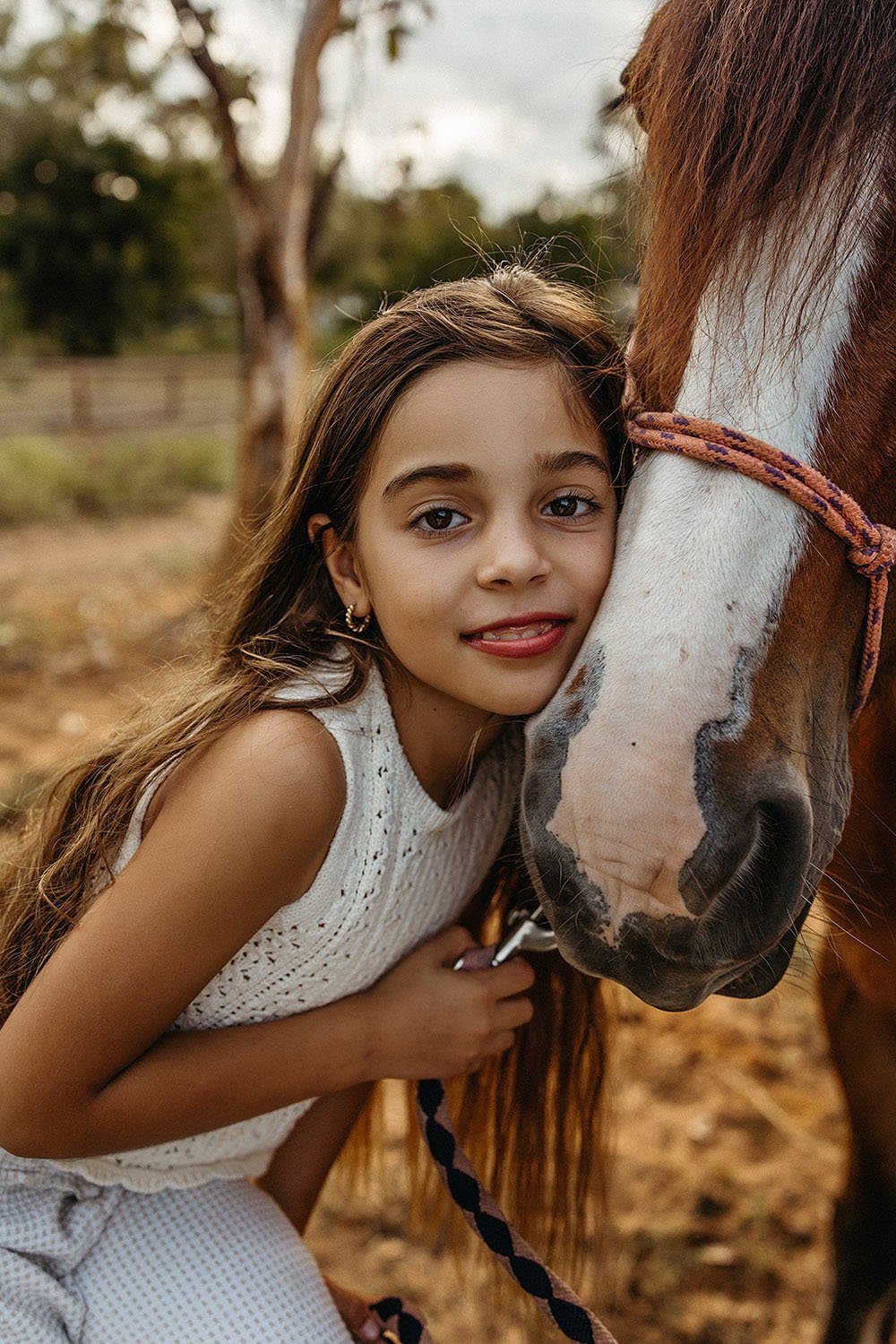 A close up of a girl with long dark hair holding a horse. Rural family photo shoot, Captured by Cody, Darwin NT.