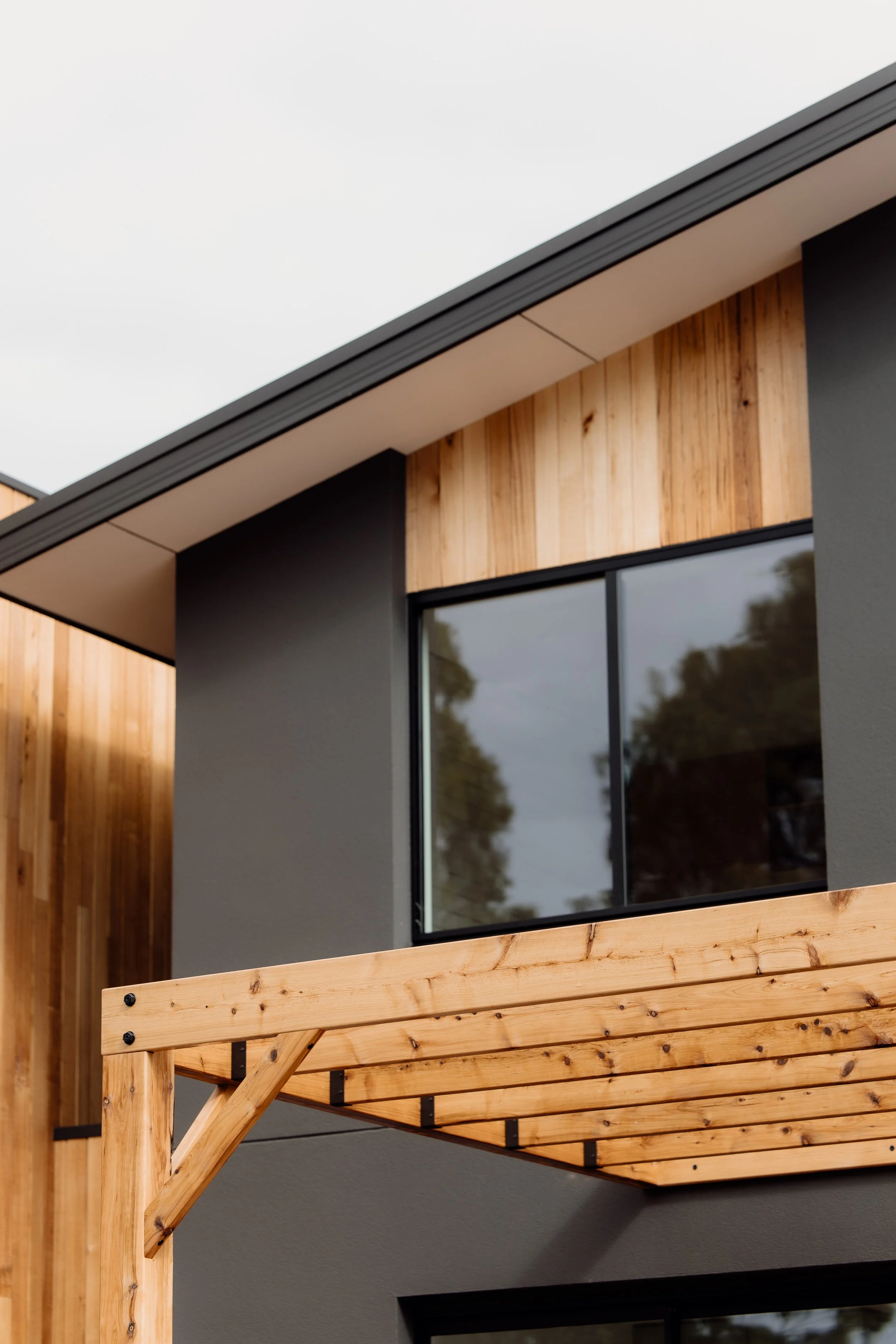 Close-up of a modern house exterior with black-framed window, wood paneling, and a newly built wooden deck.