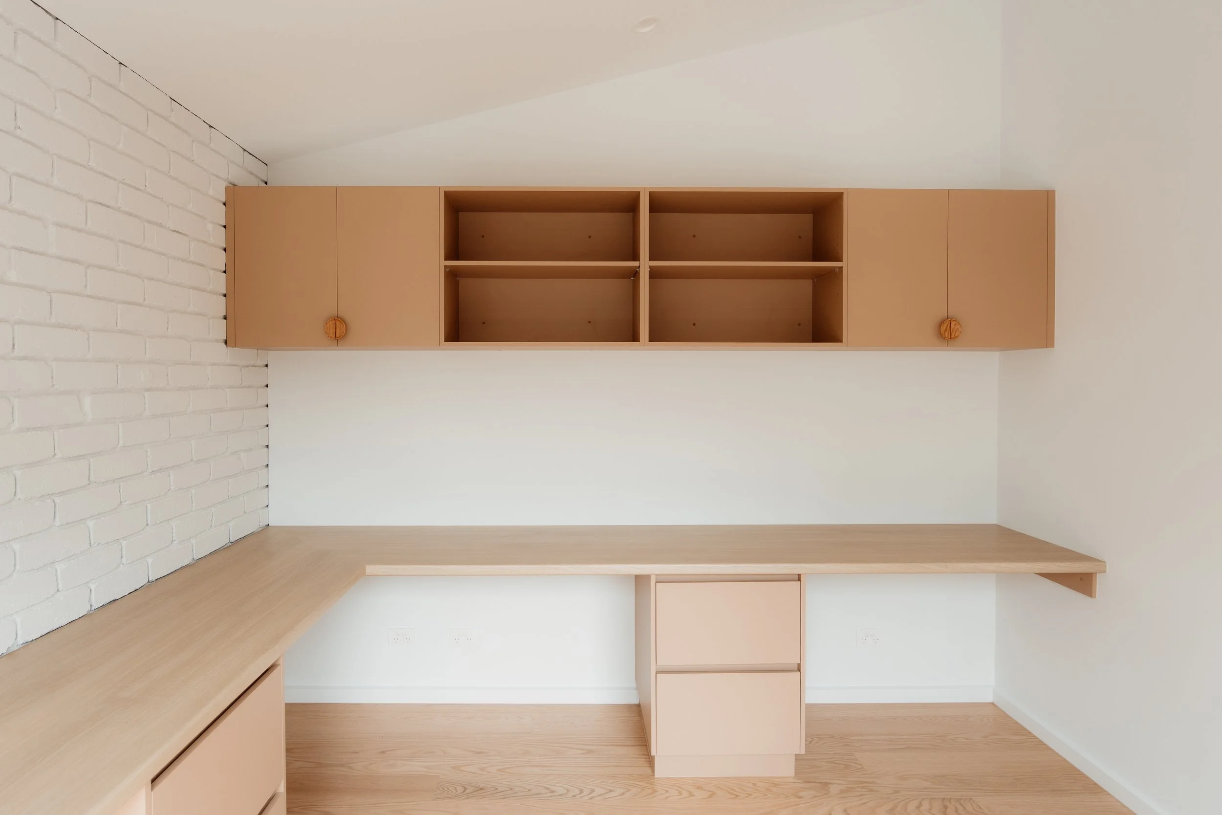 Empty kitchen with white brick wall on the left, beige cabinetry, and wooden countertops.