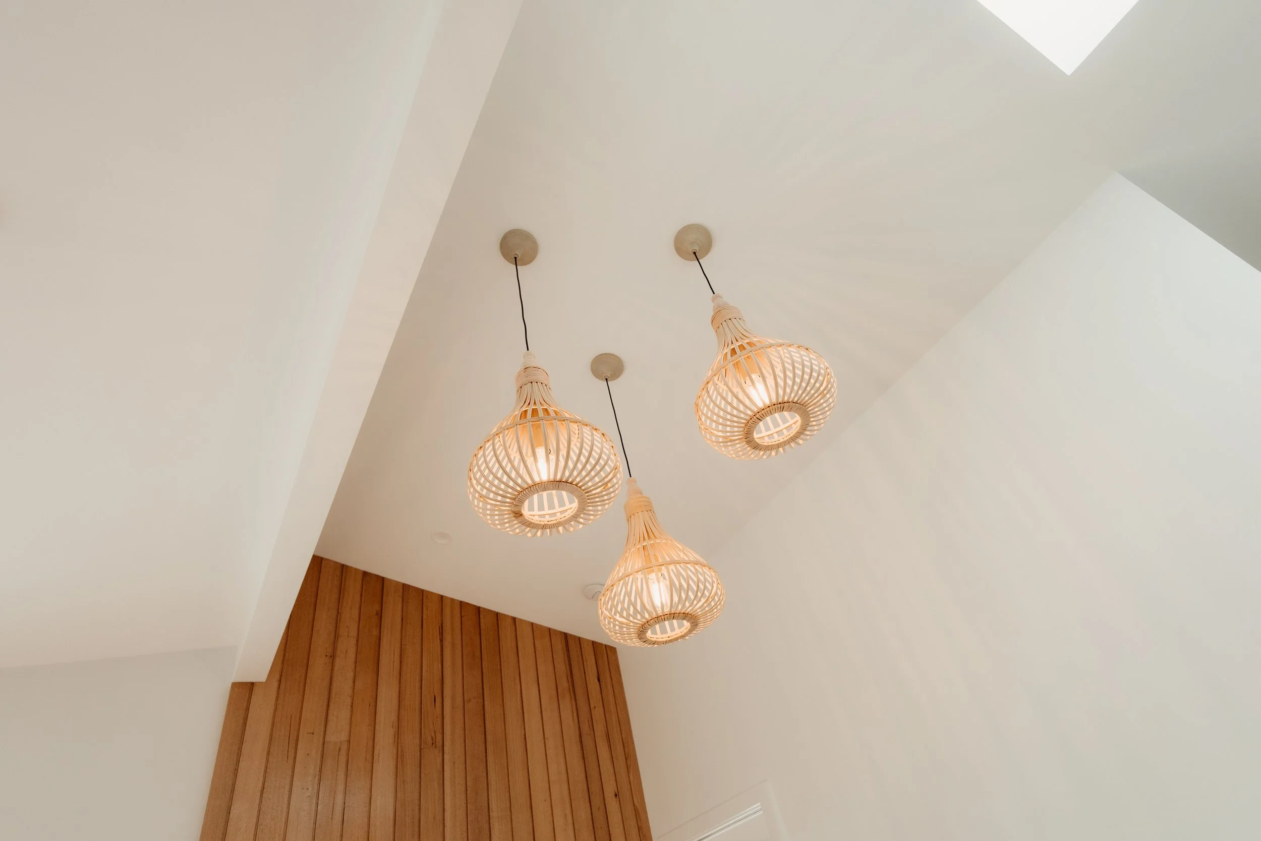 Ceiling with hanging rattan pendant light fixtures and a skylight above, with wooden wall panel on the lower part of the wall.