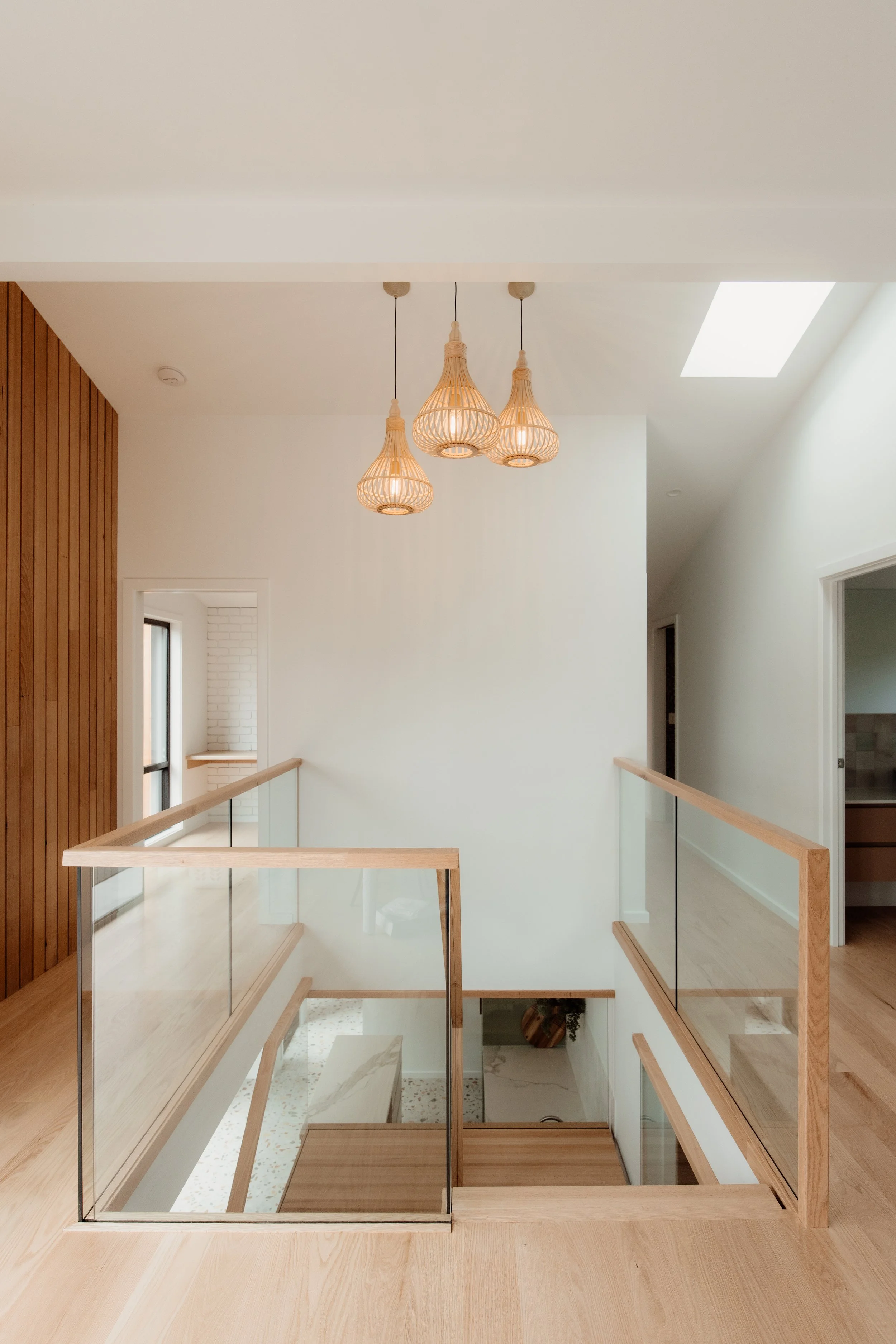 Interior view of a modern house with a staircase, hanging light fixtures, and a skylight ceiling.