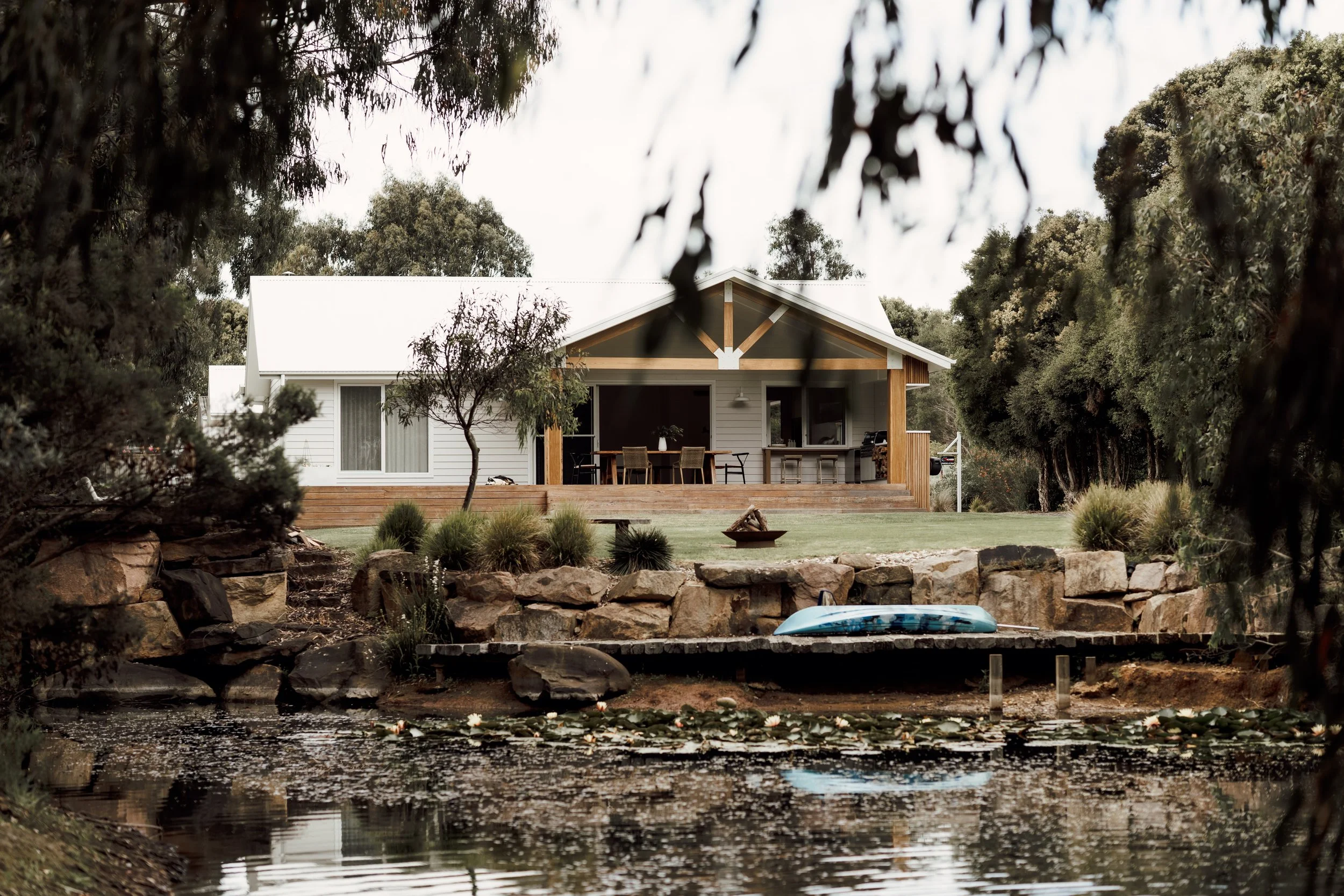 A house seen through trees, with a water body in the foreground.
