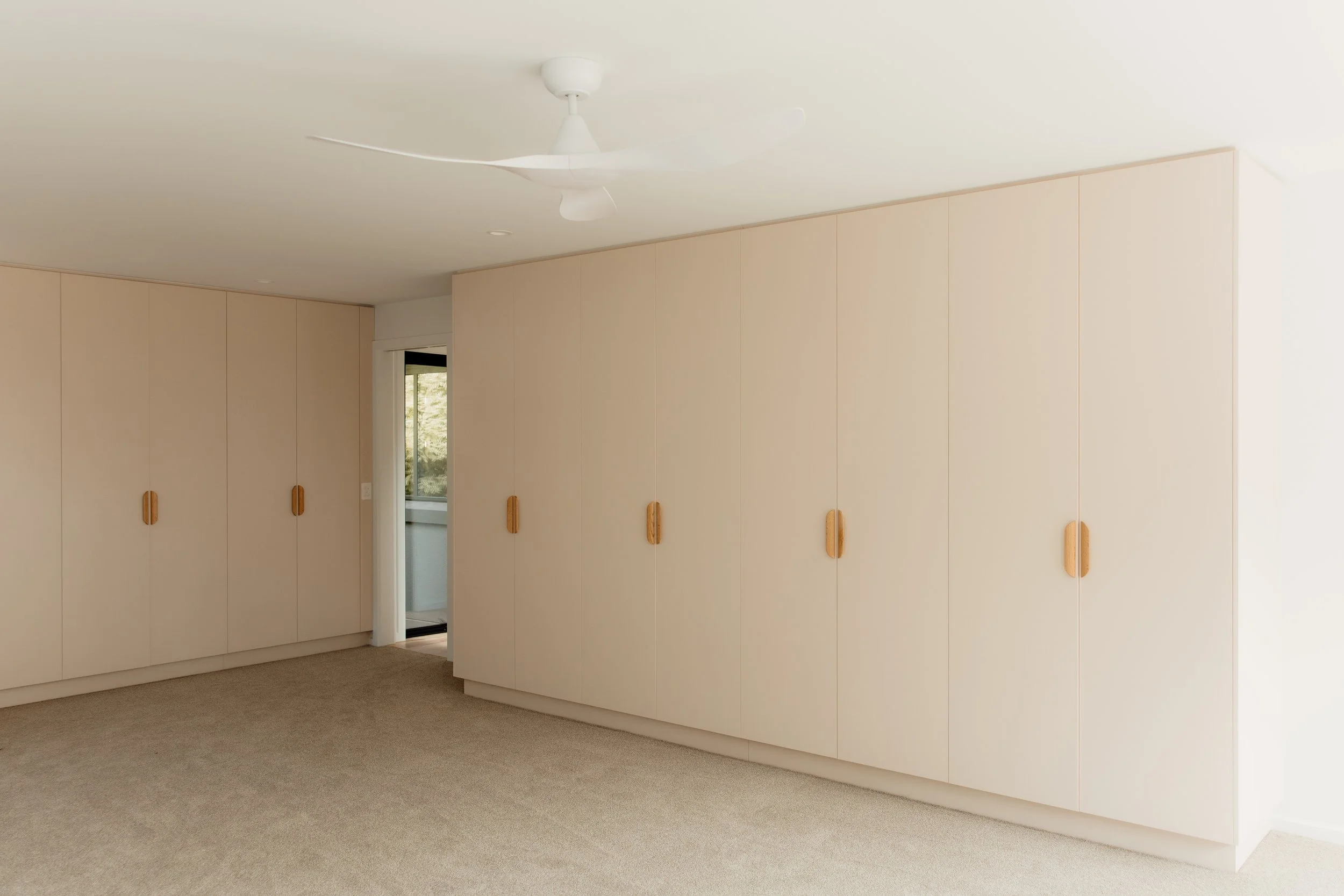 Room with beige cabinets, a ceiling fan, and a doorway leading outside, with carpeted flooring.