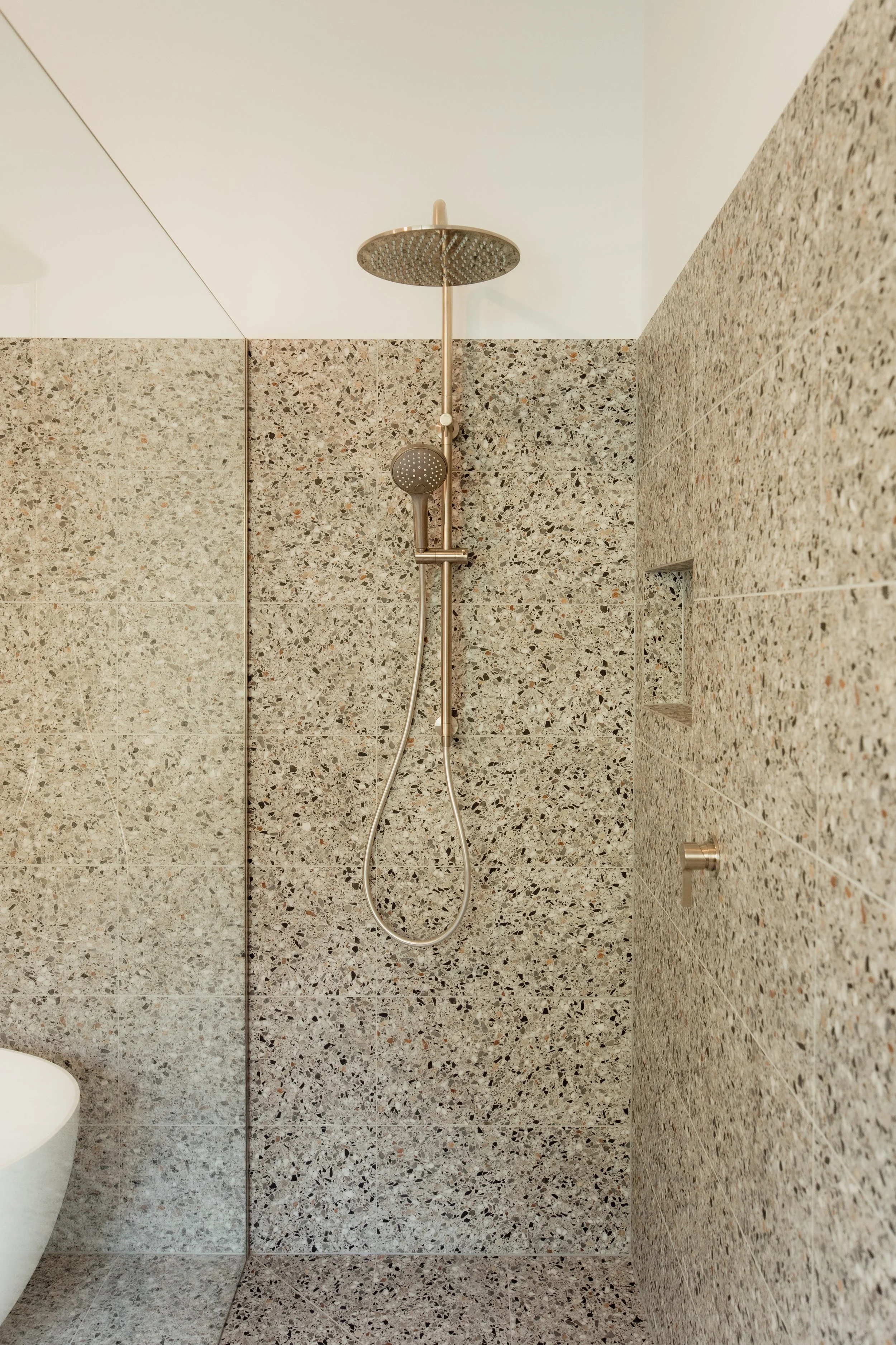 Shower with a rain shower head and handheld shower on speckled stone walls.