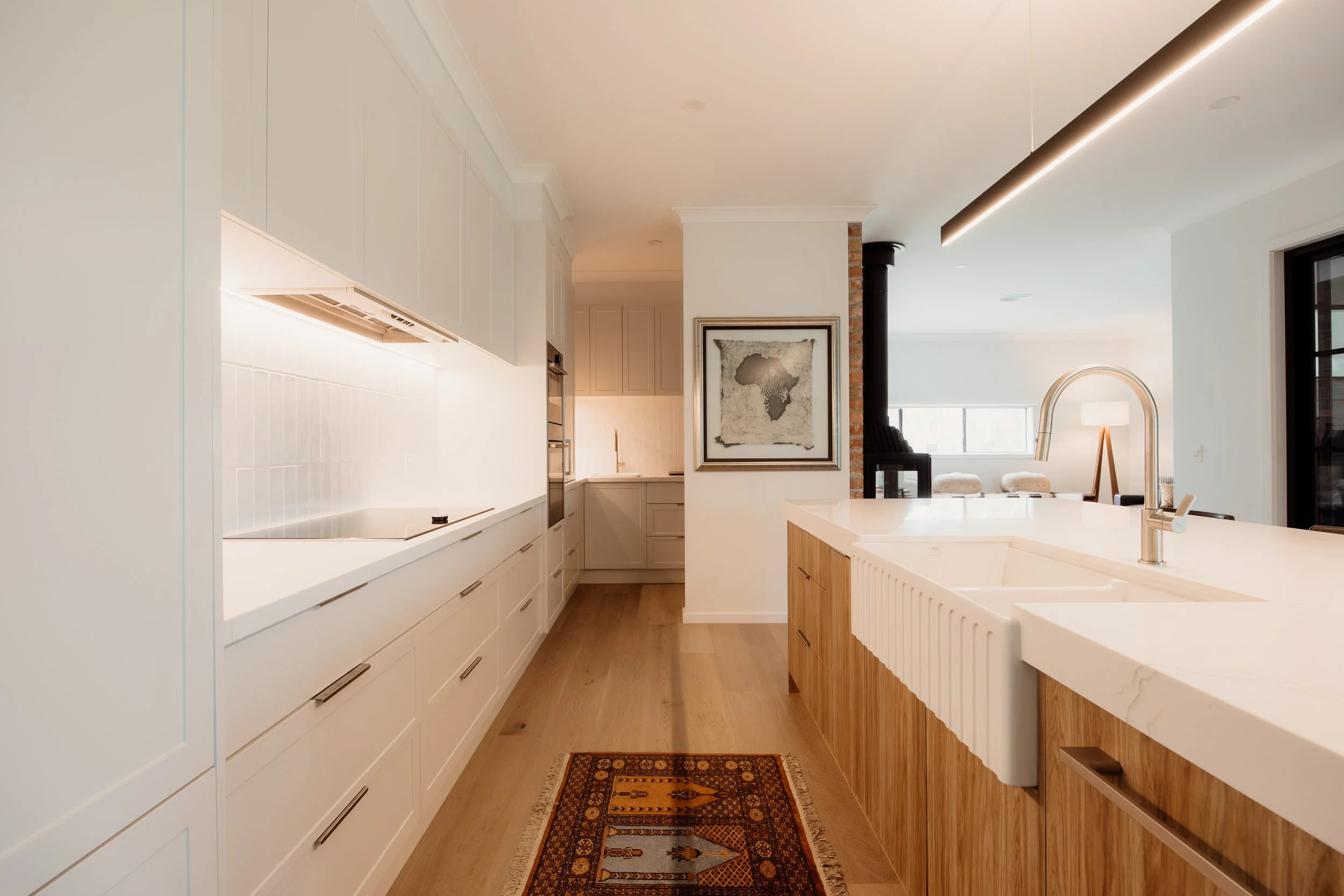 Modern kitchen with white cabinets, a wooden island, a white sink, and a framed map of Africa on the wall, illuminated by recessed lighting and natural light from windows.