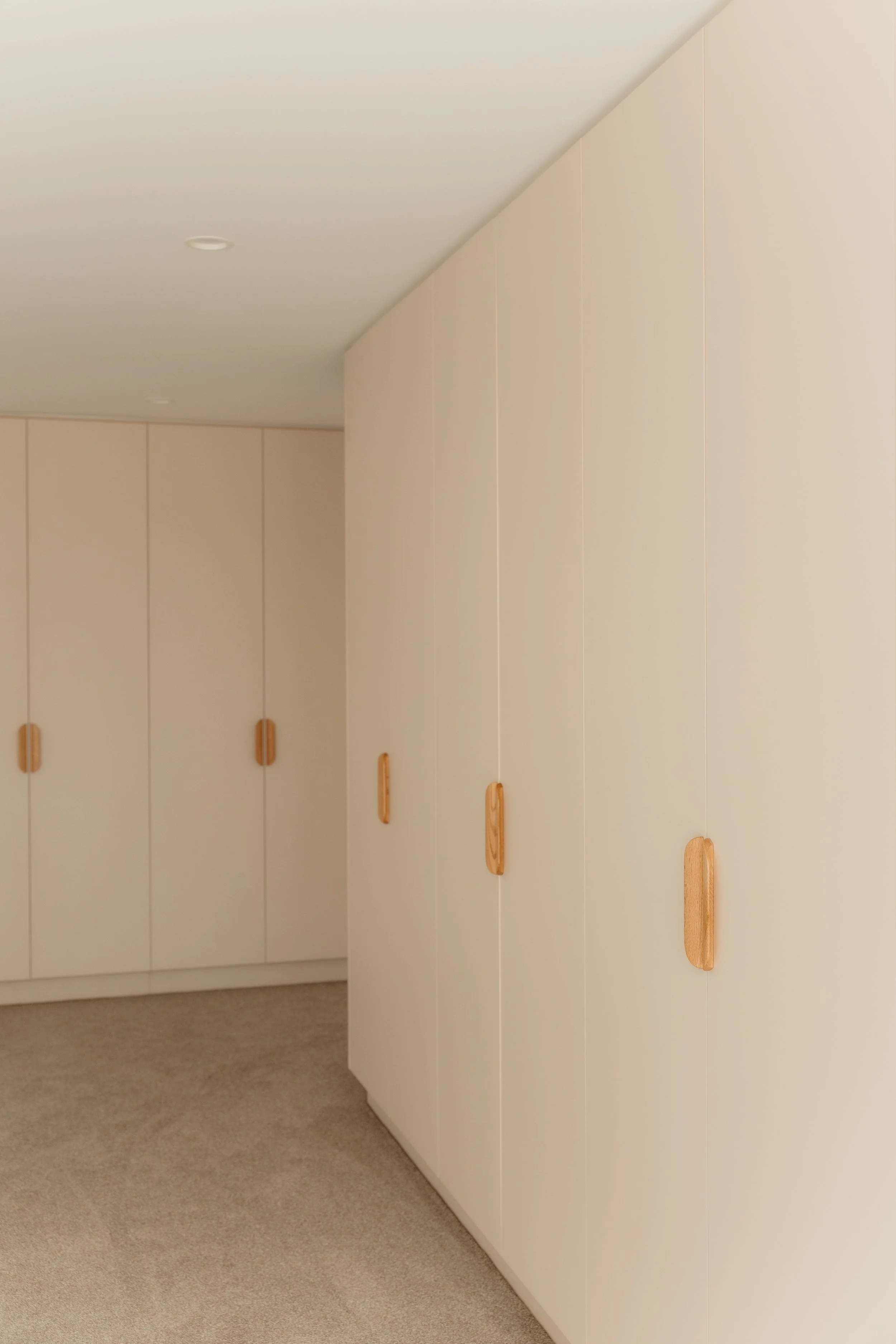 White storage cabinets with wooden handles in a room with beige carpet and a white ceiling.