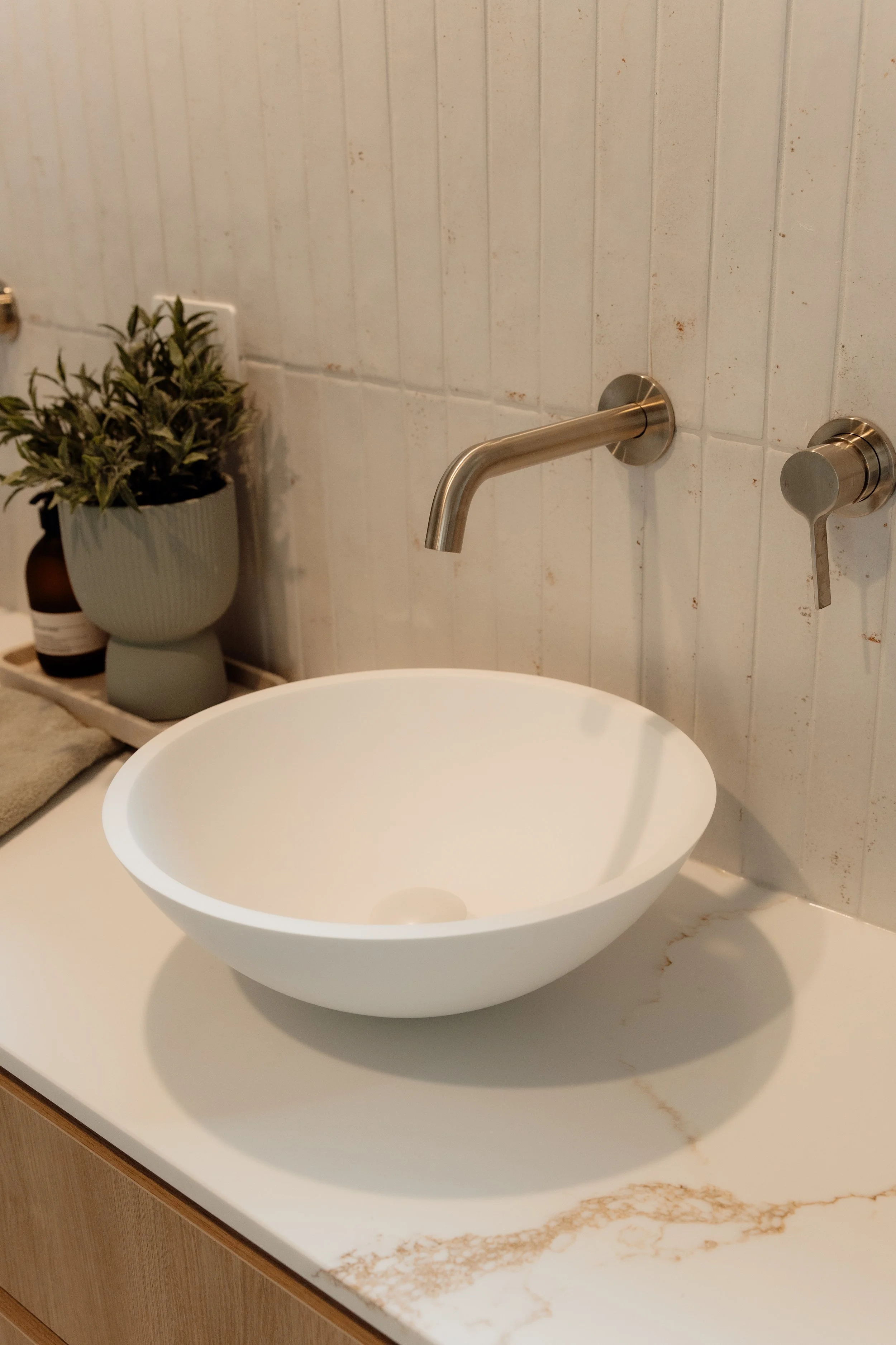 Bathroom sink with a modern metal faucet, a potted plant on a tray, and a beige marble countertop.