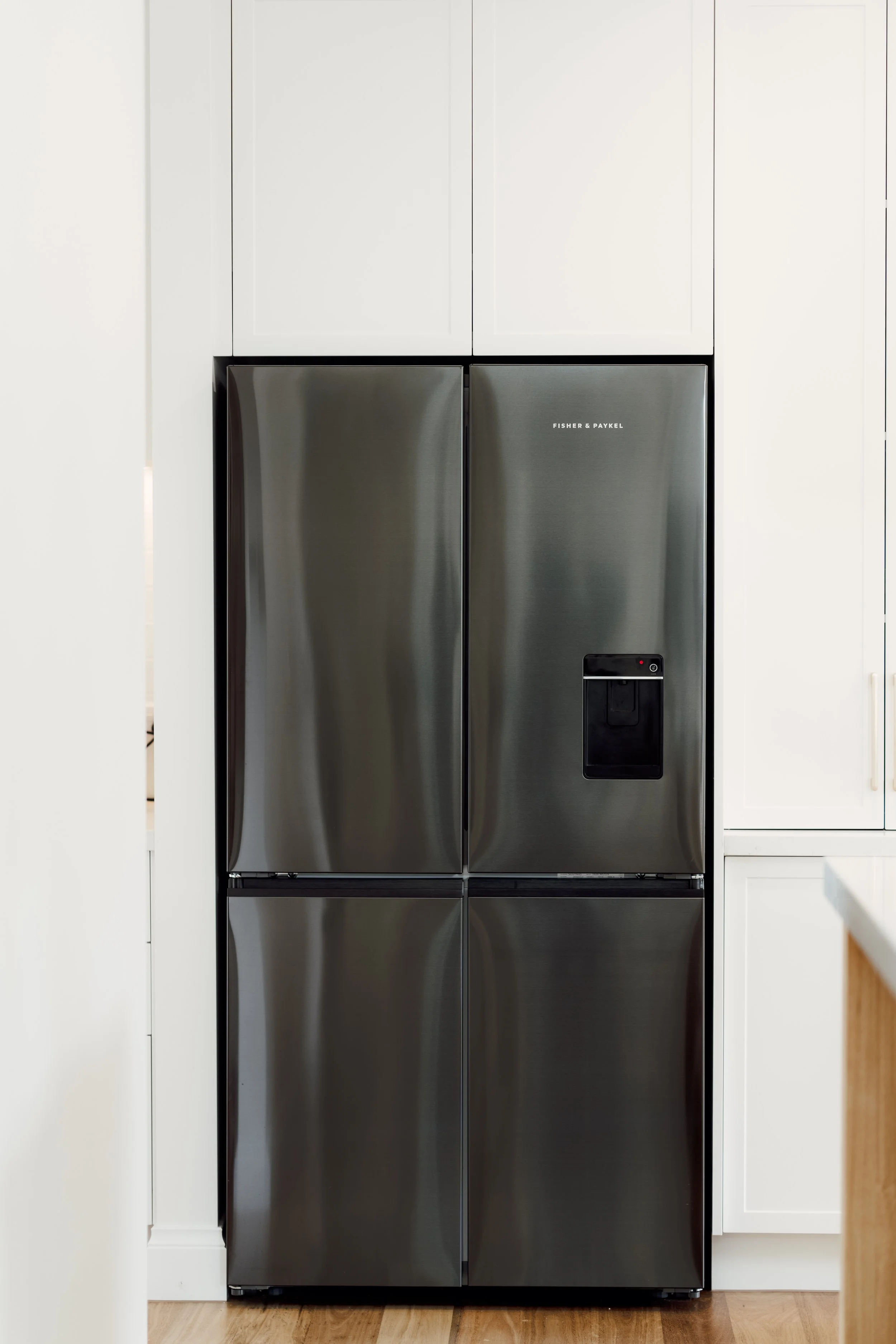 Stainless steel Fisher & Paykel refrigerator in a modern kitchen with white cabinets and hardwood floors.