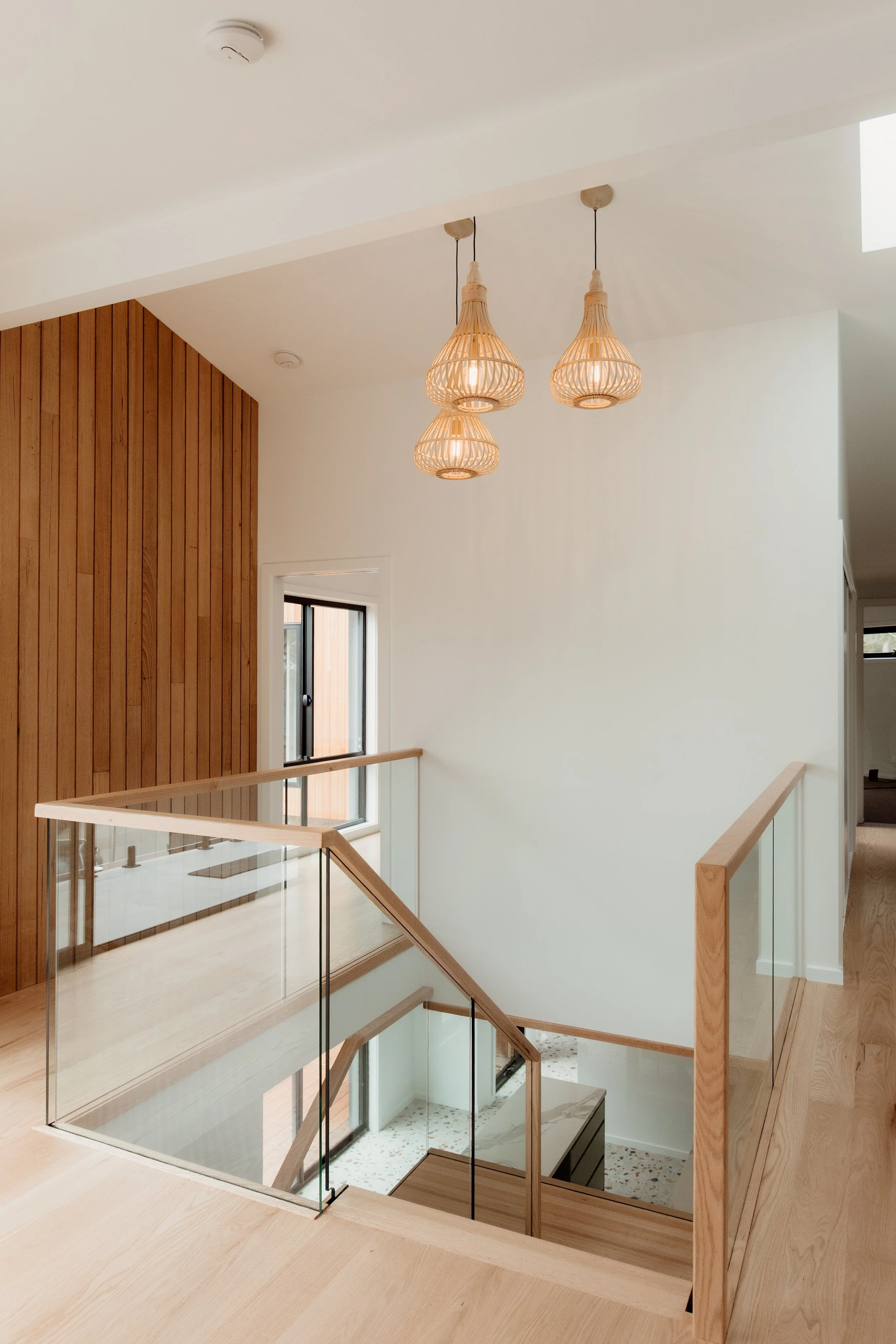Interior view of a modern multi-level home with wooden and glass railings, a staircase leading down, and pendant lights hanging from the ceiling.